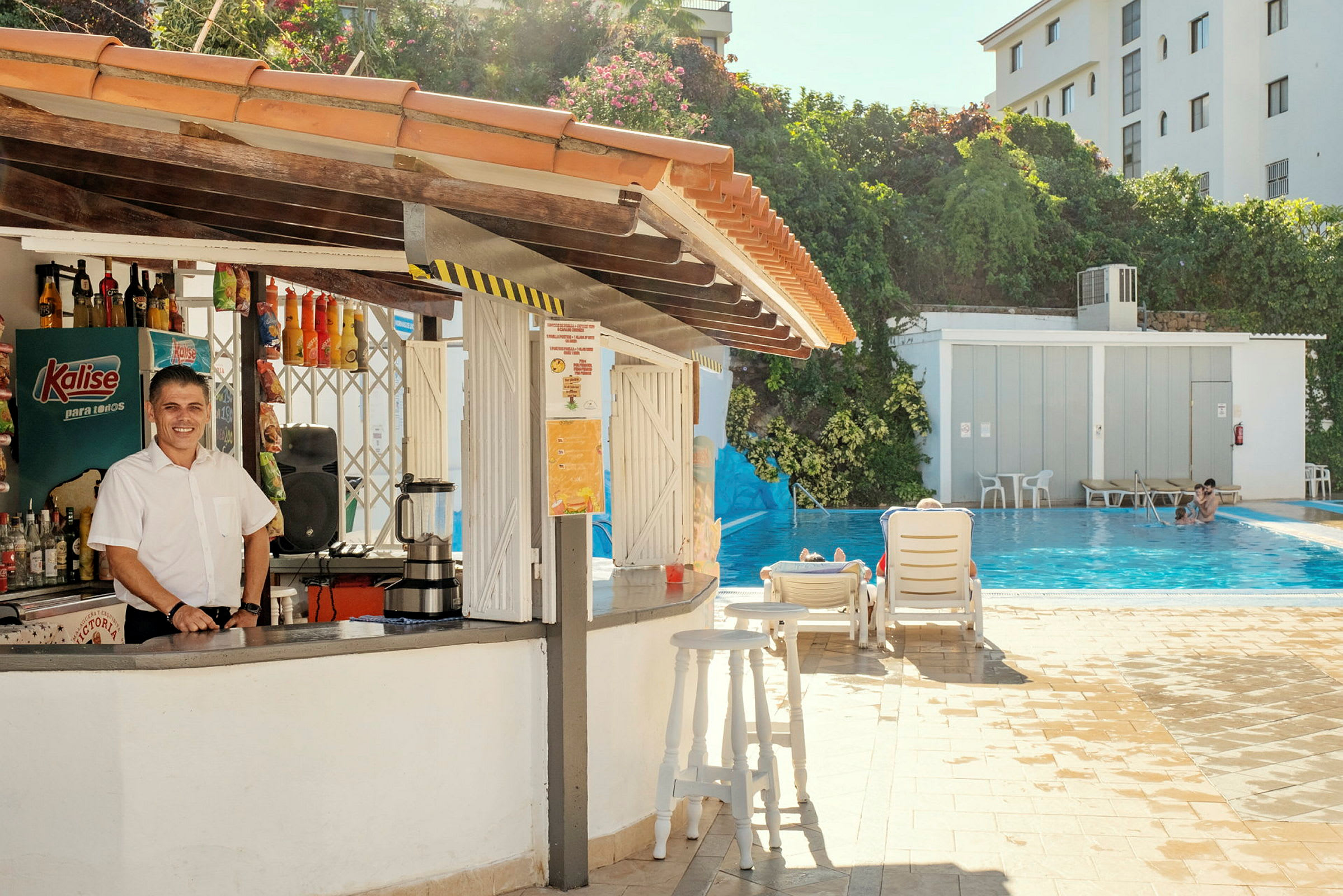 Utomhusbar vid en pool med solstolar och grönska i bakgrunden. (AI-genererad text)