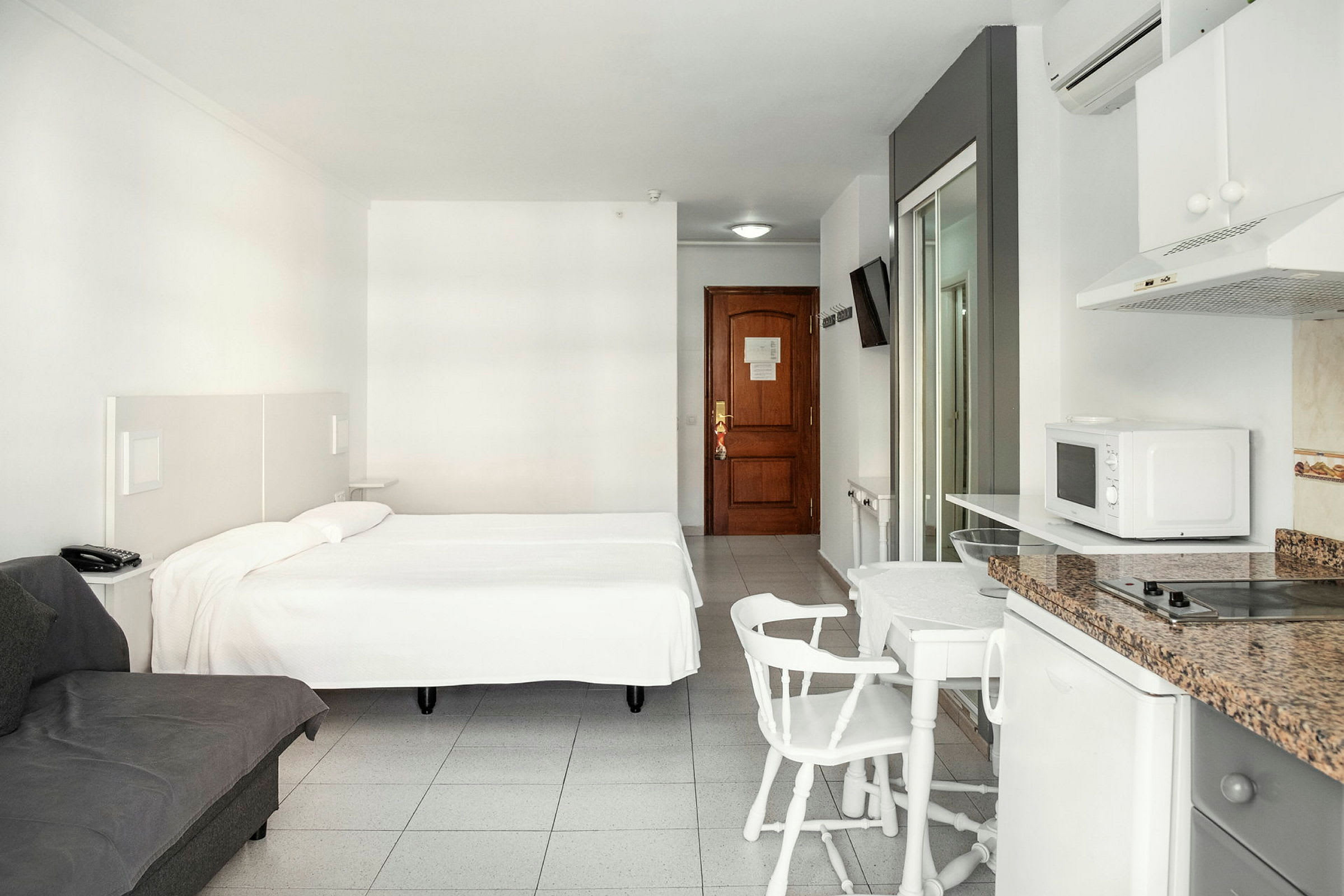 Ett hotellrum med en dubbelsäng, en soffa, matbord med stolar och ett pentry. (AI-genererad text)