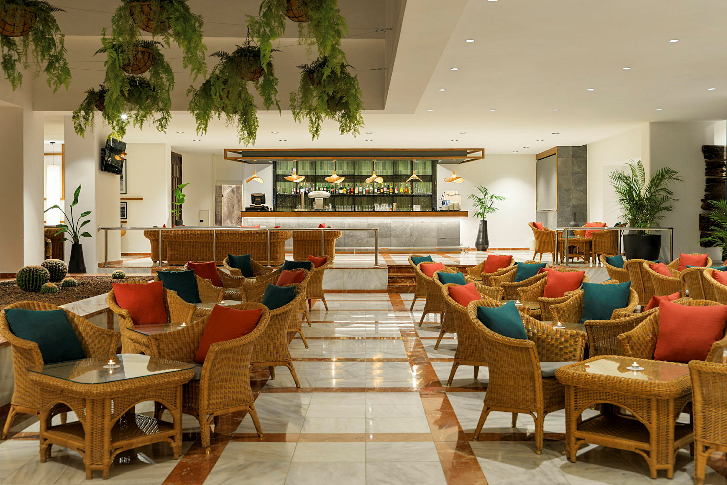 Restaurang eller loungeområde med flätade stolar, bord och färgglada kuddar samt en bar i bakgrunden. (AI-genererad text)