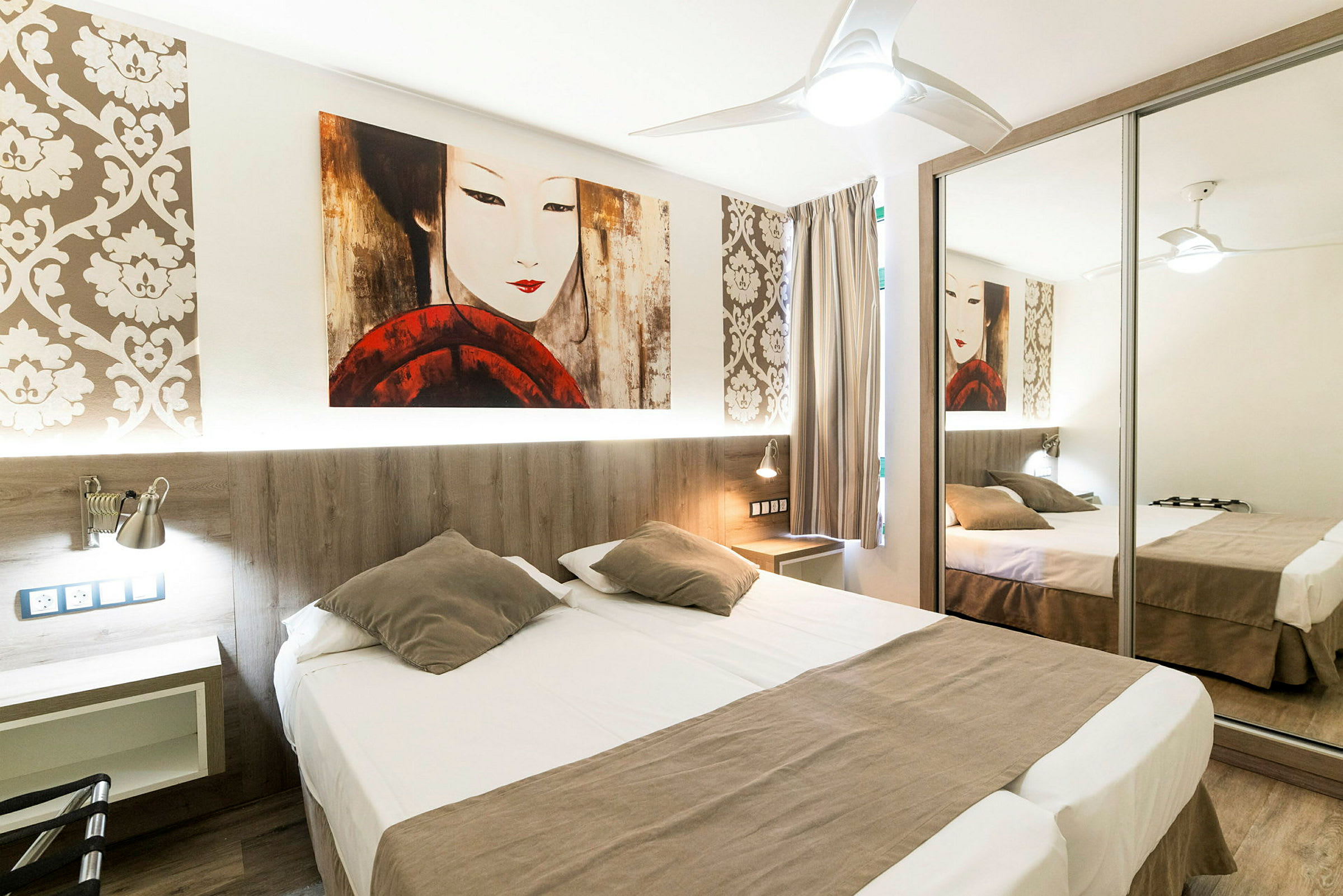 Ett hotellrum med en dubbelsäng, spegelgarderob och dekorativ väggtapet. (AI-genererad text)