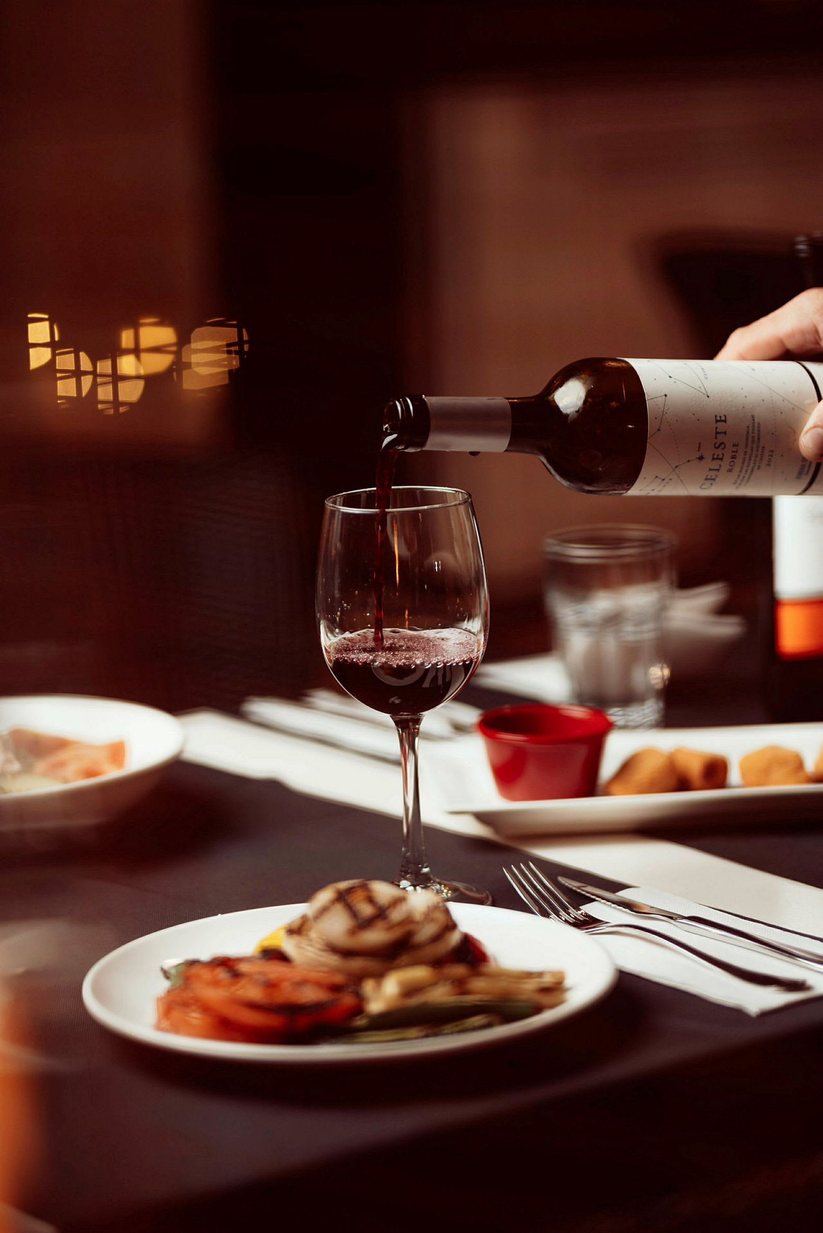 En person häller vin i ett glas som står på ett dukat bord. (AI-genererad text)