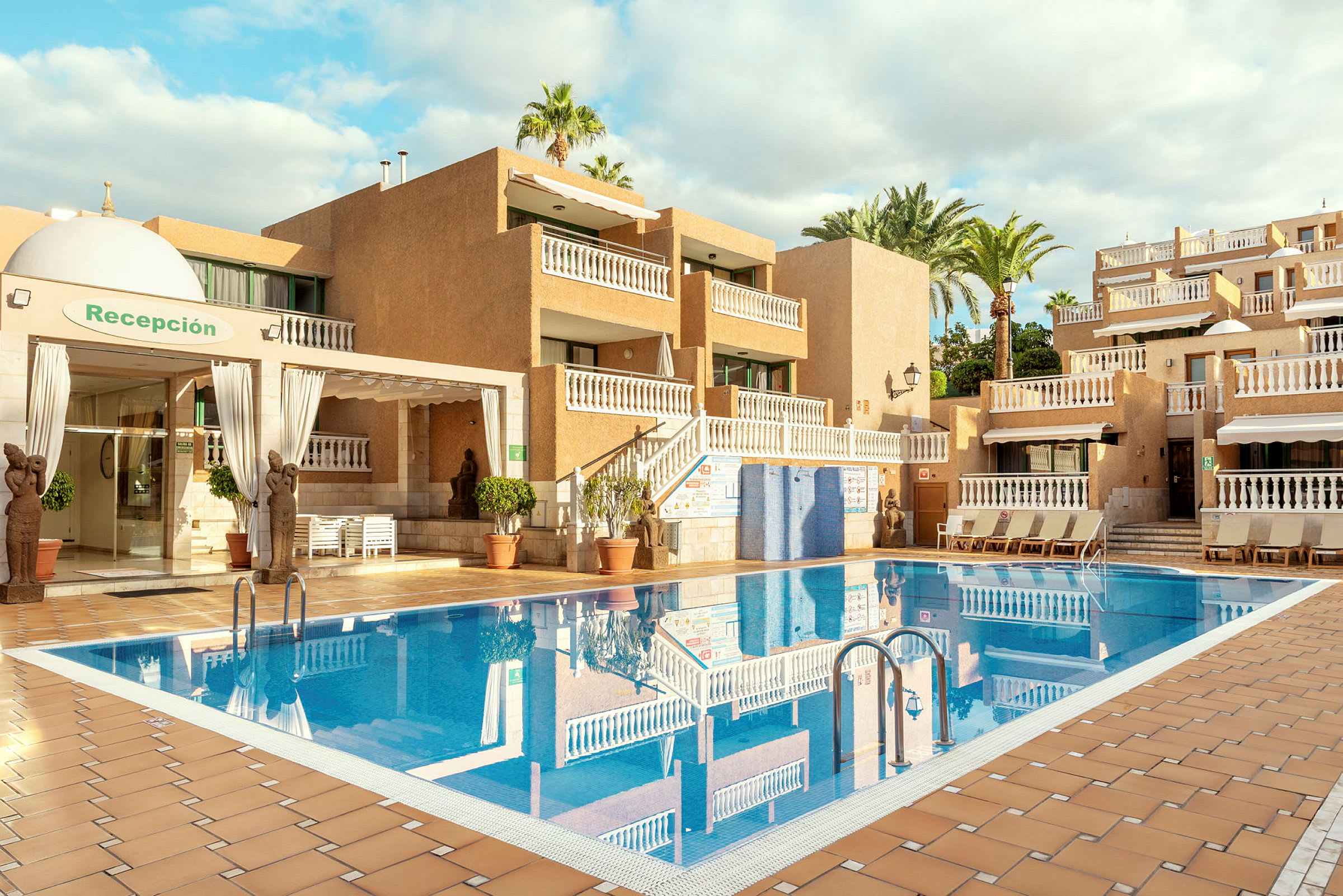 Ett hotellområde med pool, omgivna av byggnader och palmer. (AI-genererad text)