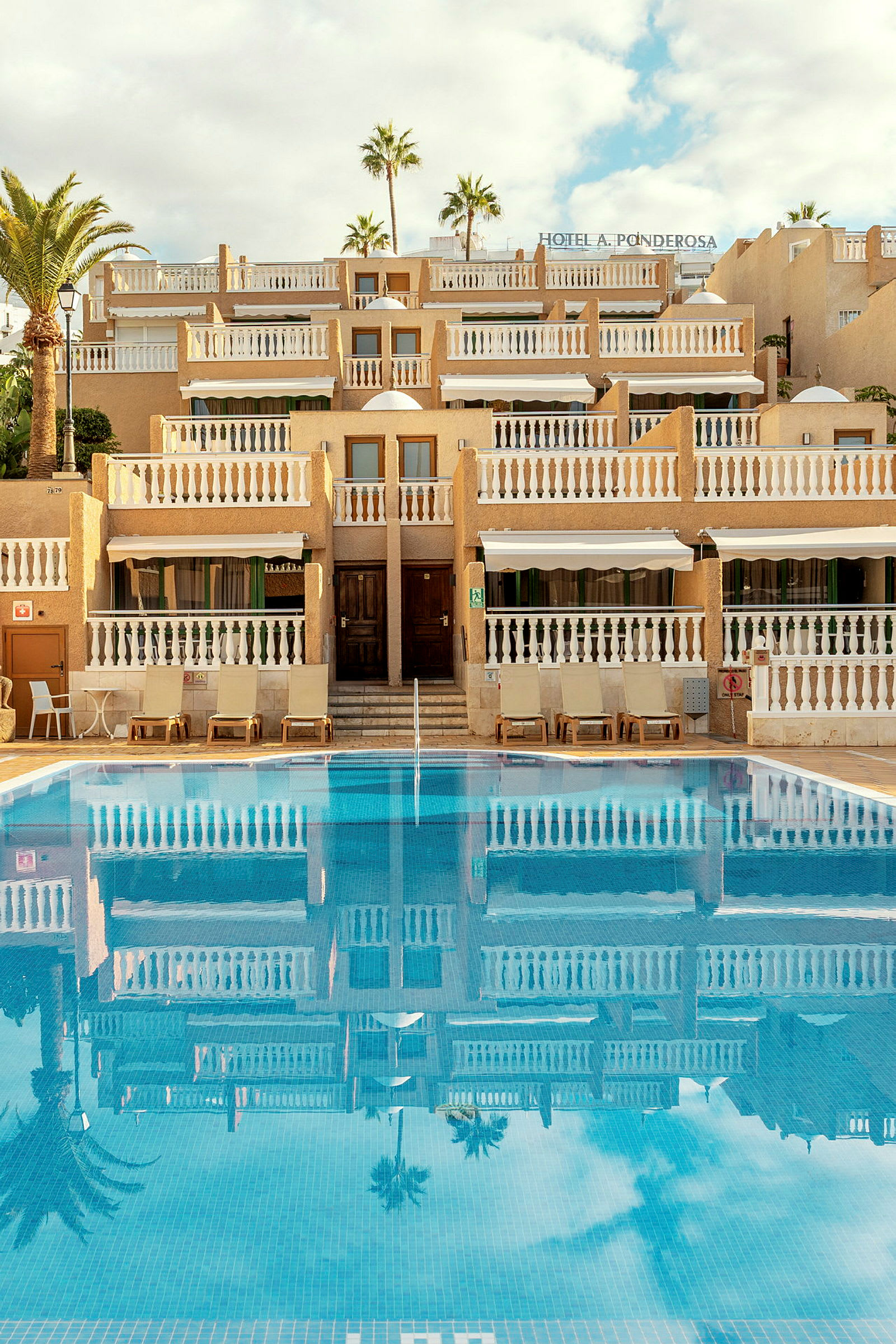 Bild av ett hotell med flera våningar och symmetriska balkonger, bredvid en klarblå pool. (AI-genererad text)