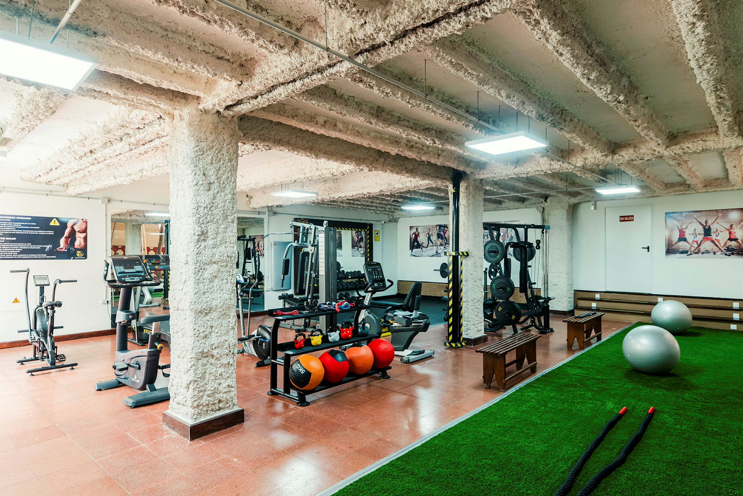 Ett gym med träningsmaskiner, vikter, medicinbollar, mattor och pilatesbollar. (AI-genererad text)