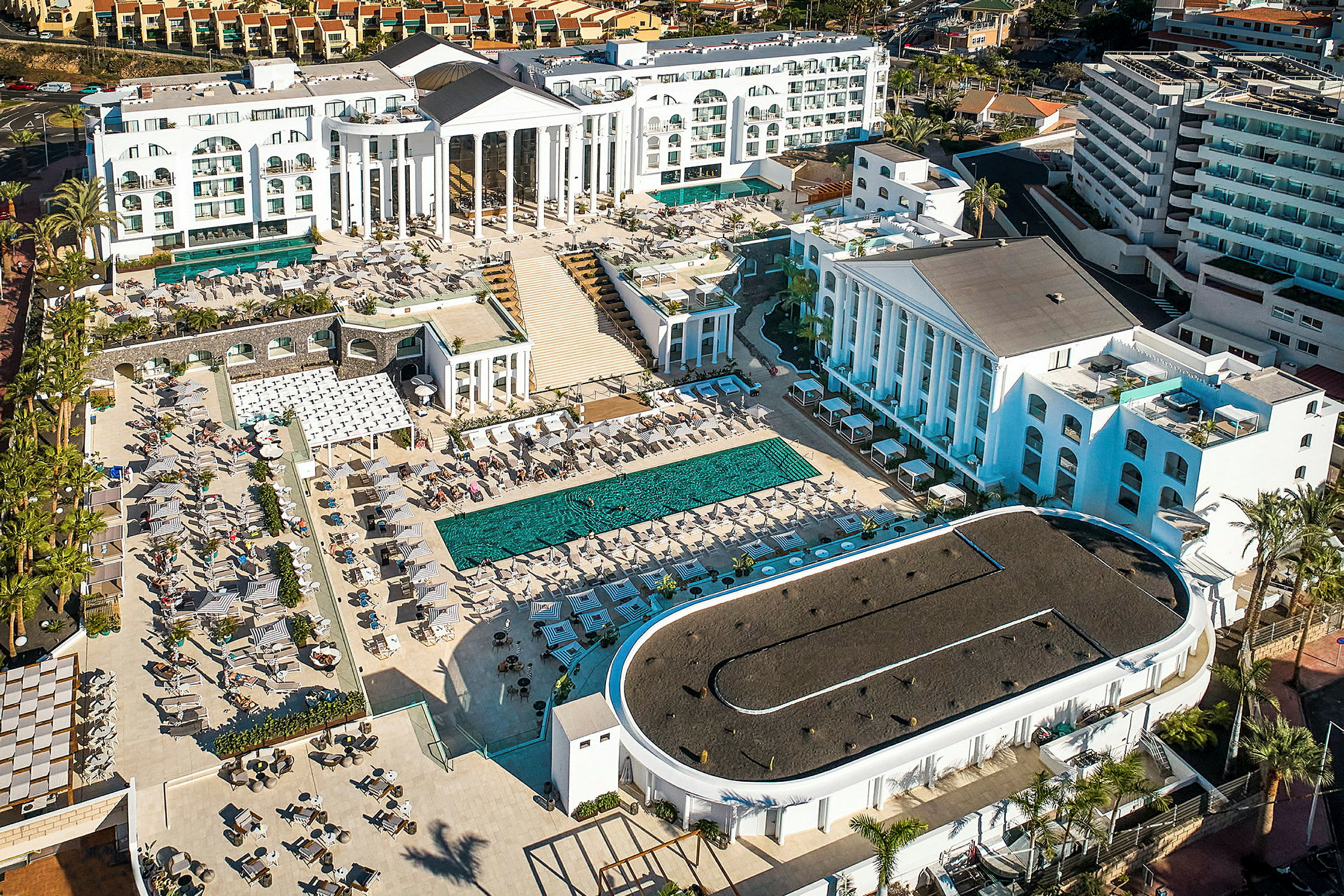 Flygfoto av ett större hotellkomplex med pool och solstolar. (AI-genererad text)