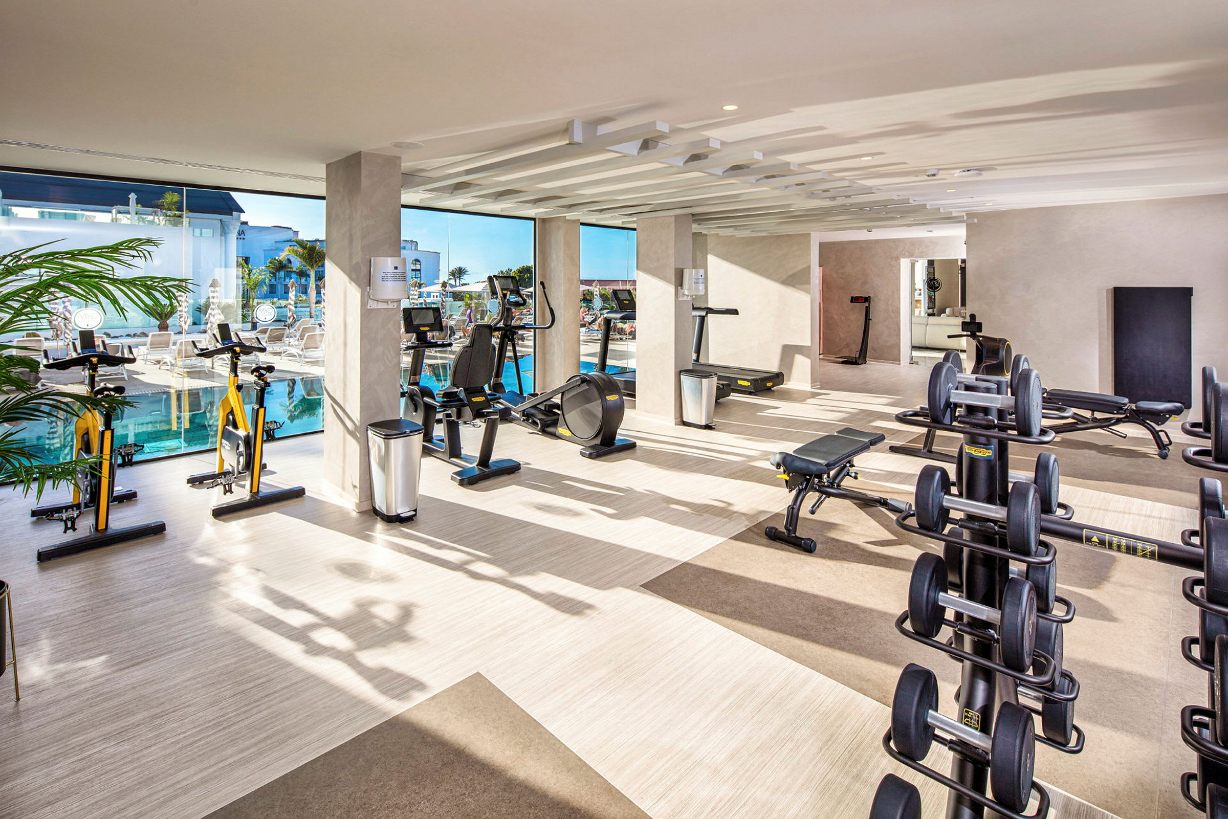 Ett gym med träningsutrustning och stora fönster som vetter mot en pool. (AI-genererad text)