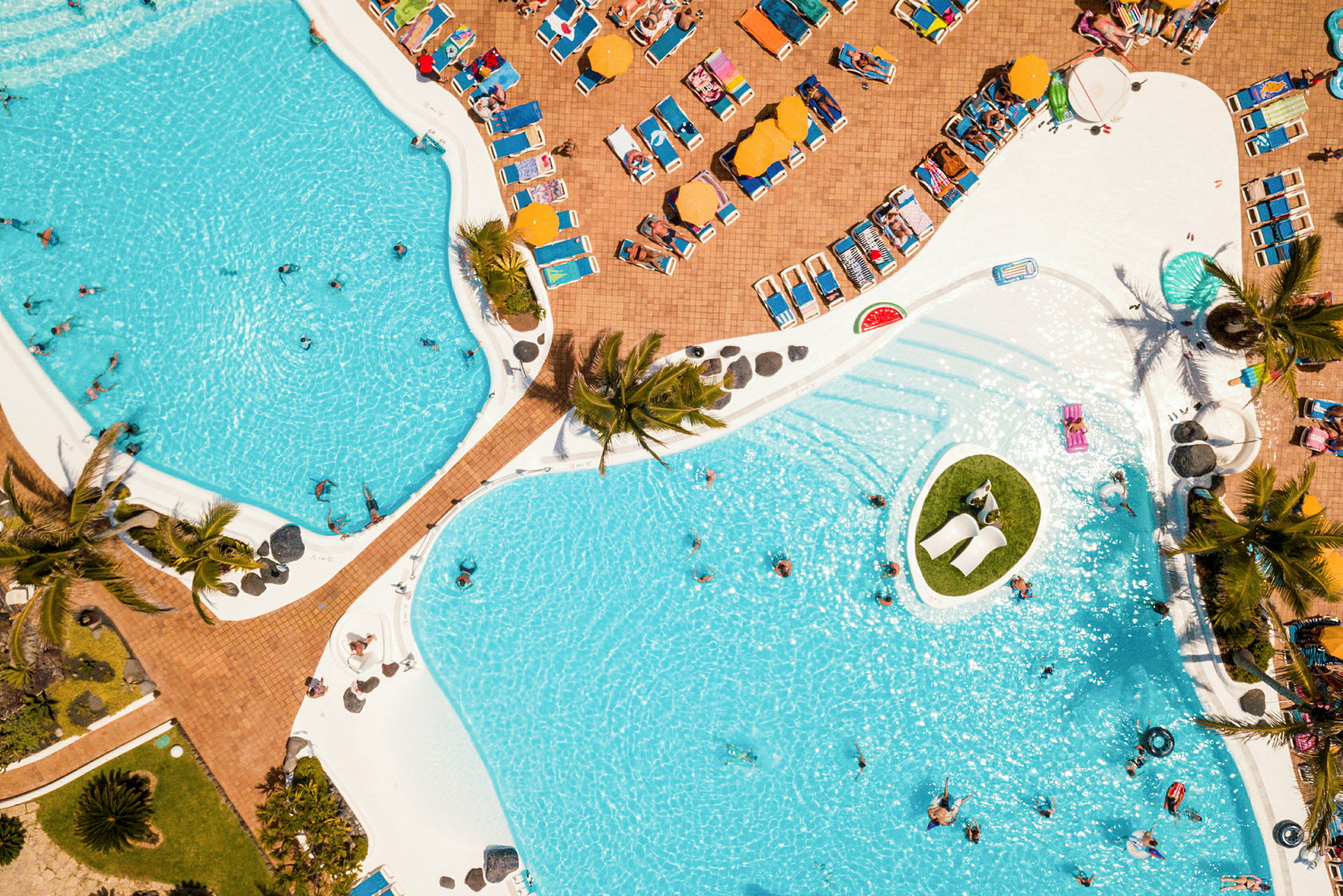 Flygbild av en stor pool områdesdel, omgiven av solstolar och parasoller. (AI-genererad text)