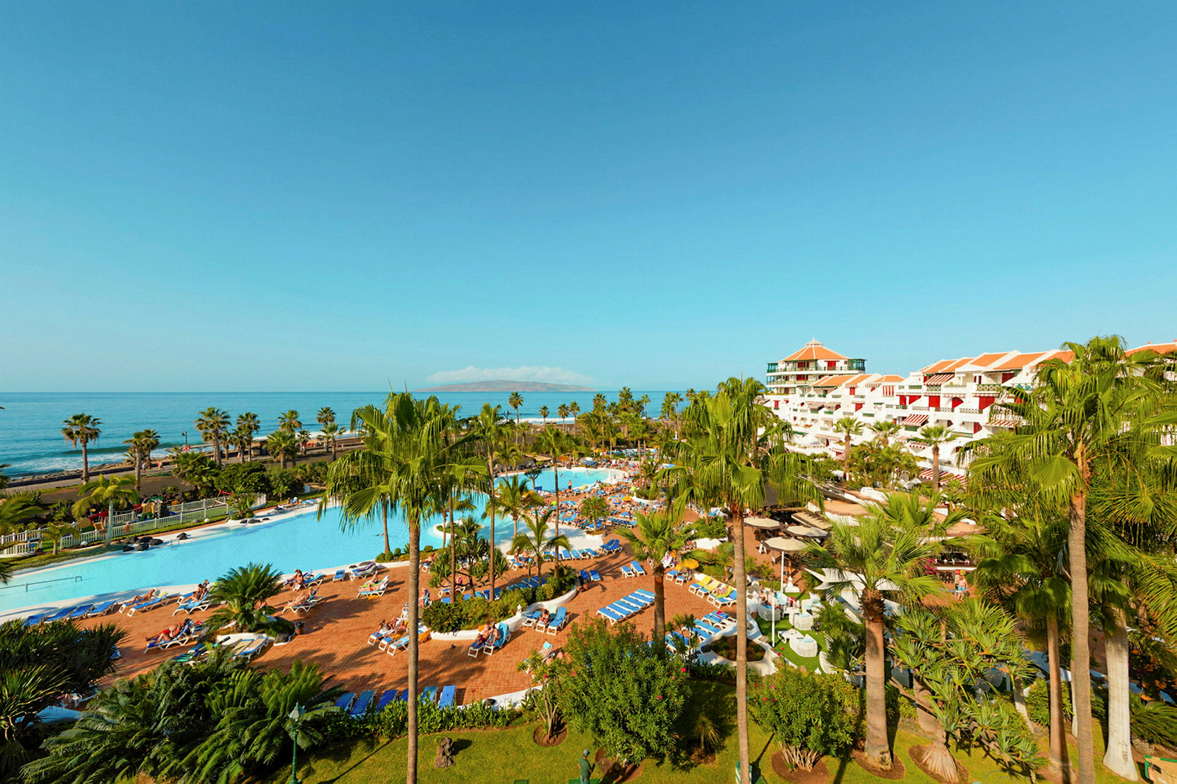 Resort med poolområde, palmer och havet i bakgrunden. (AI-genererad text)