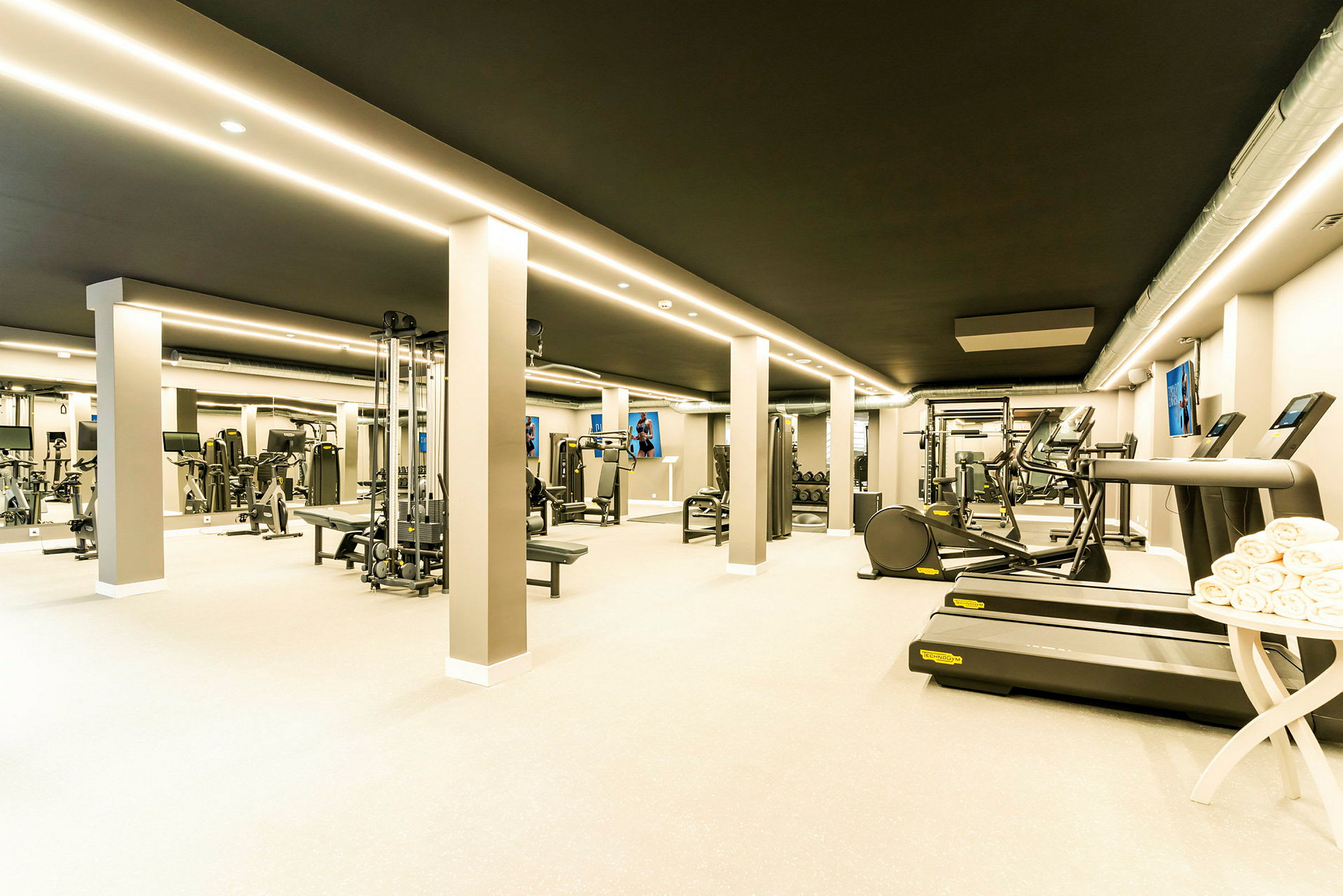 Ett modernt gym med olika träningsmaskiner och utrustning, samt löpband och handdukar vid sidan. (AI-genererad text)