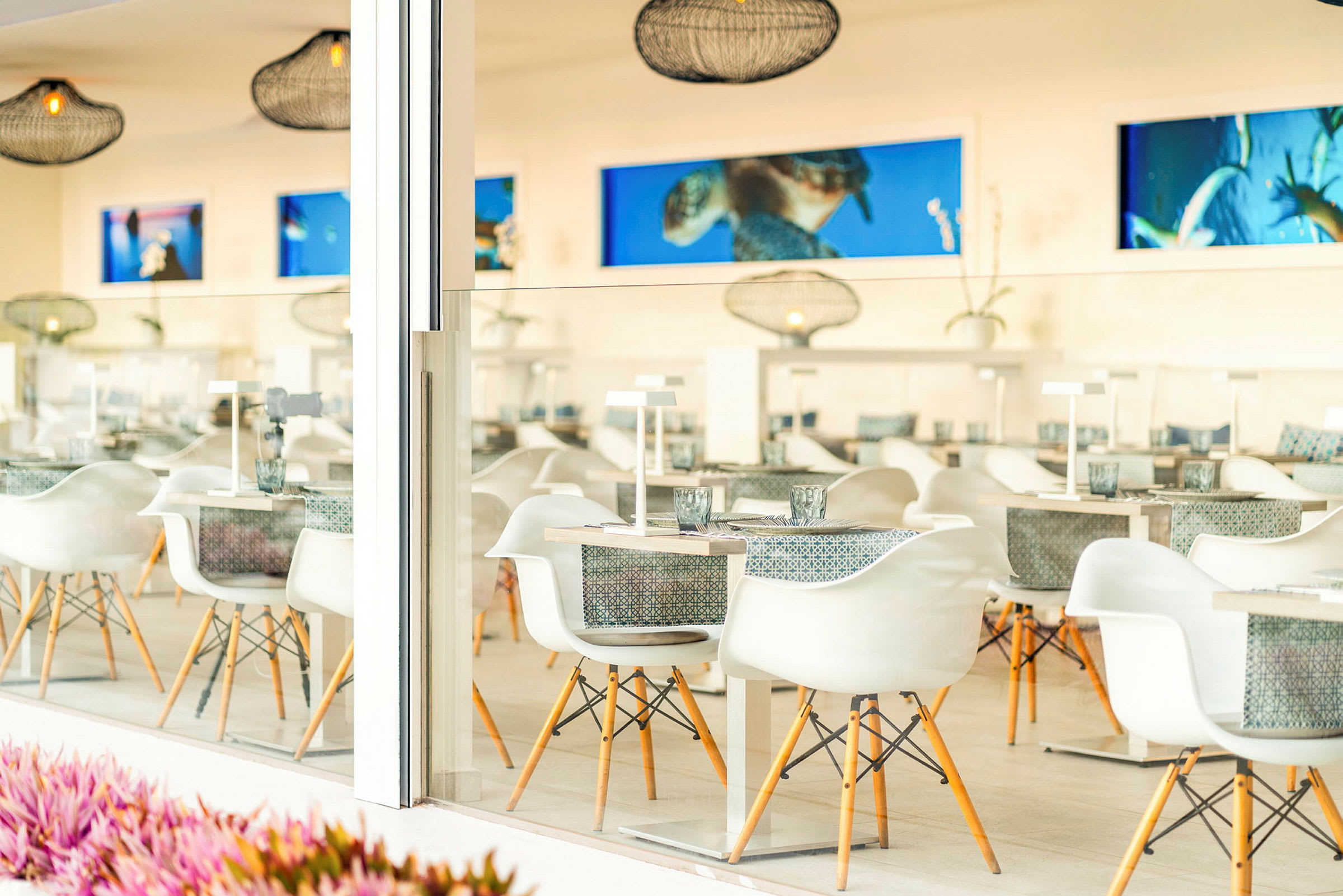 En modern och ljus restaurang med vita stolar och dukade bord, dekorerad med hängande lampor och konstverk på väggarna. (AI-genererad text)