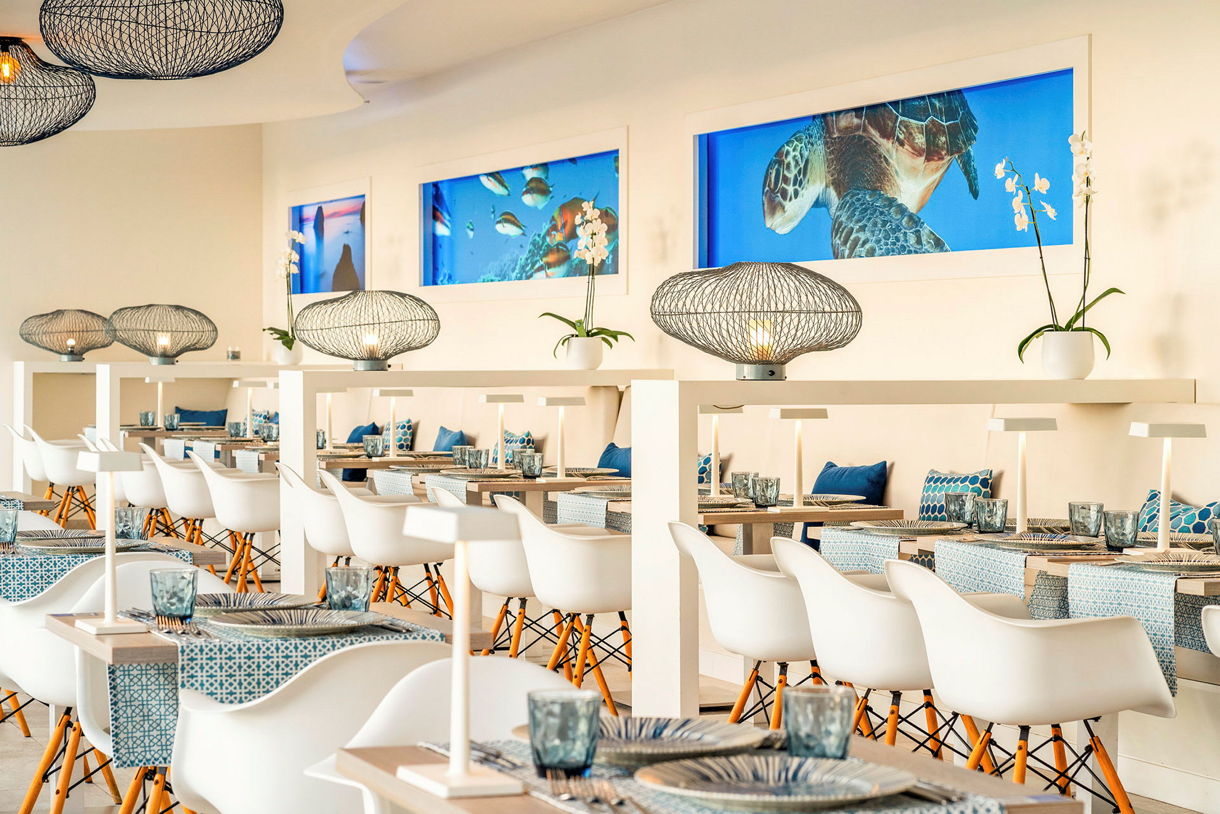 Inredning av en ljus och modern restaurang med stilfulla bord, vita stolar, dekorativa lampor och marina inslag. (AI-genererad text)