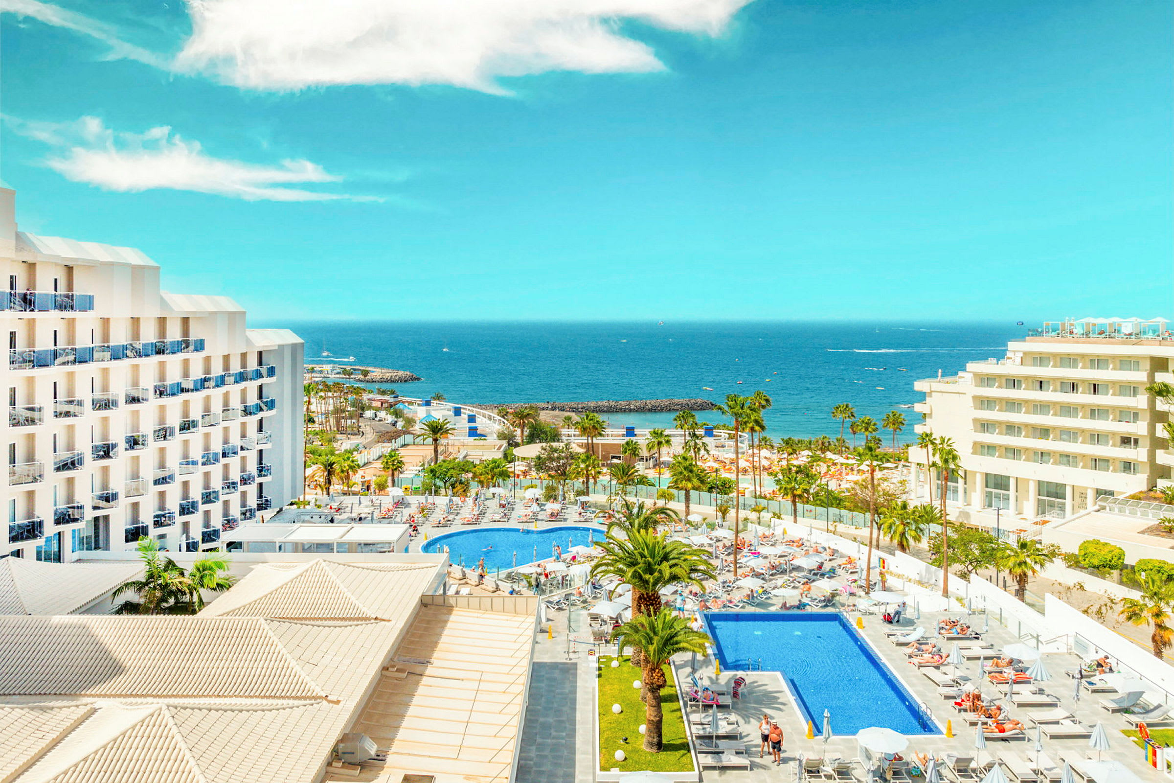 Hotell med poolområde och palmer vid kusten med havsutsikt. (AI-genererad text)