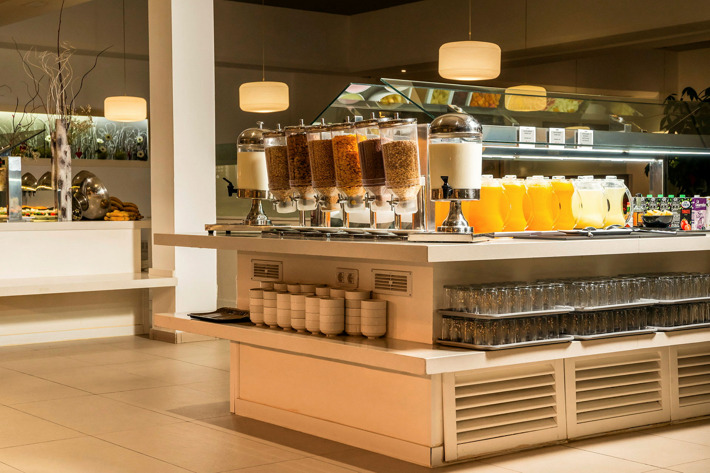 Buffébord med olika frukostalternativ, inkluderande spannmålsbehållare, mjölkdispenser, juicekanna och glas. (AI-genererad text)