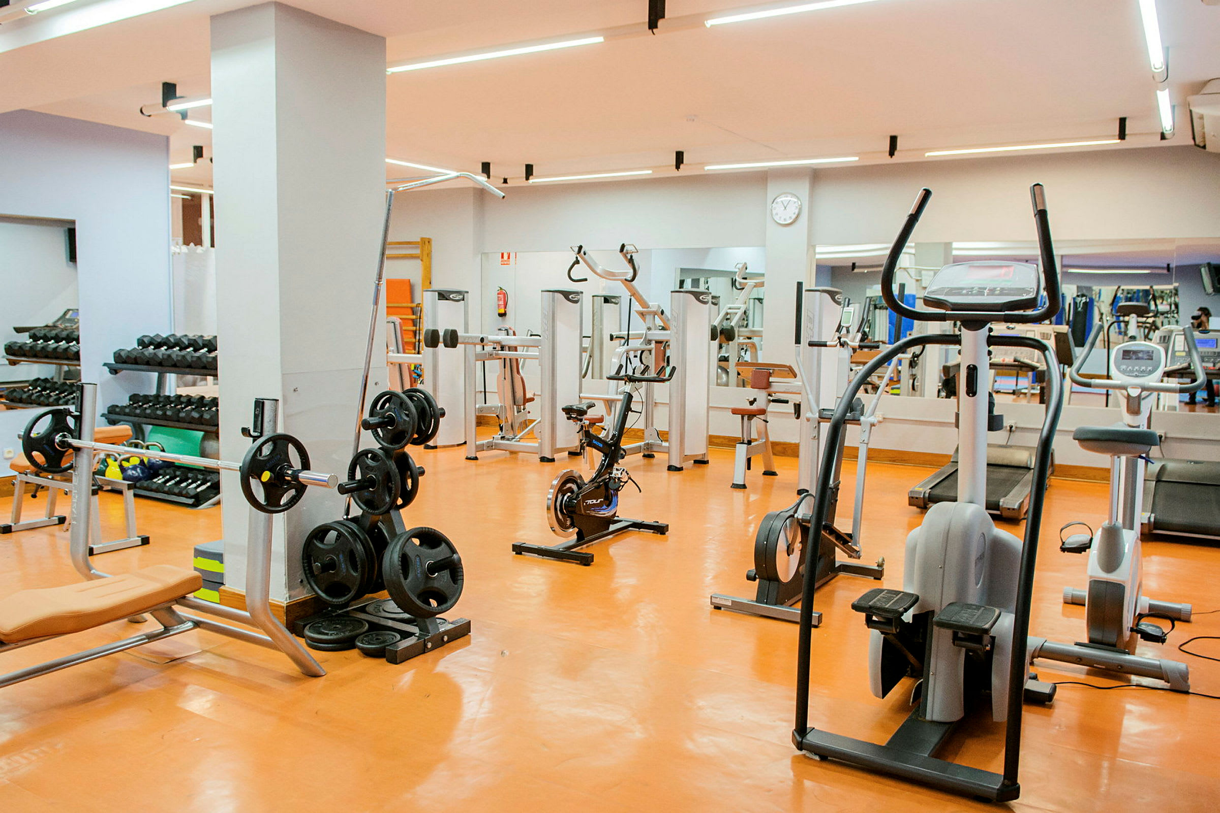 Ett fullt utrustat gym med träningsredskap och maskiner. Tydliga speglar syns i bakgrunden. (AI-genererad text)