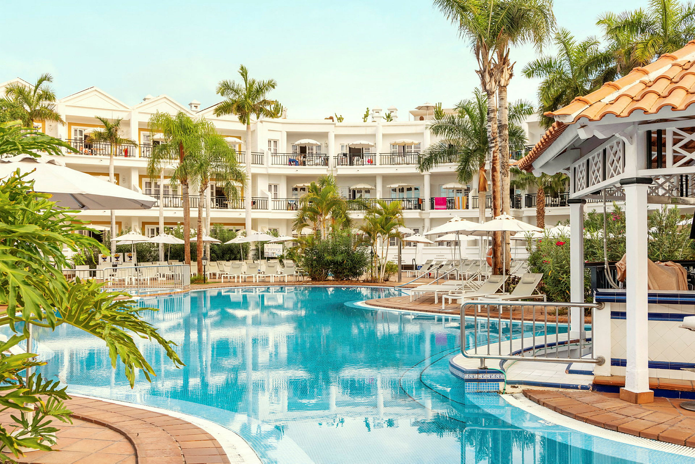 Bild av ett hotell med en pool, omgiven av solstolar, parasoller och grönska. (AI-genererad text)