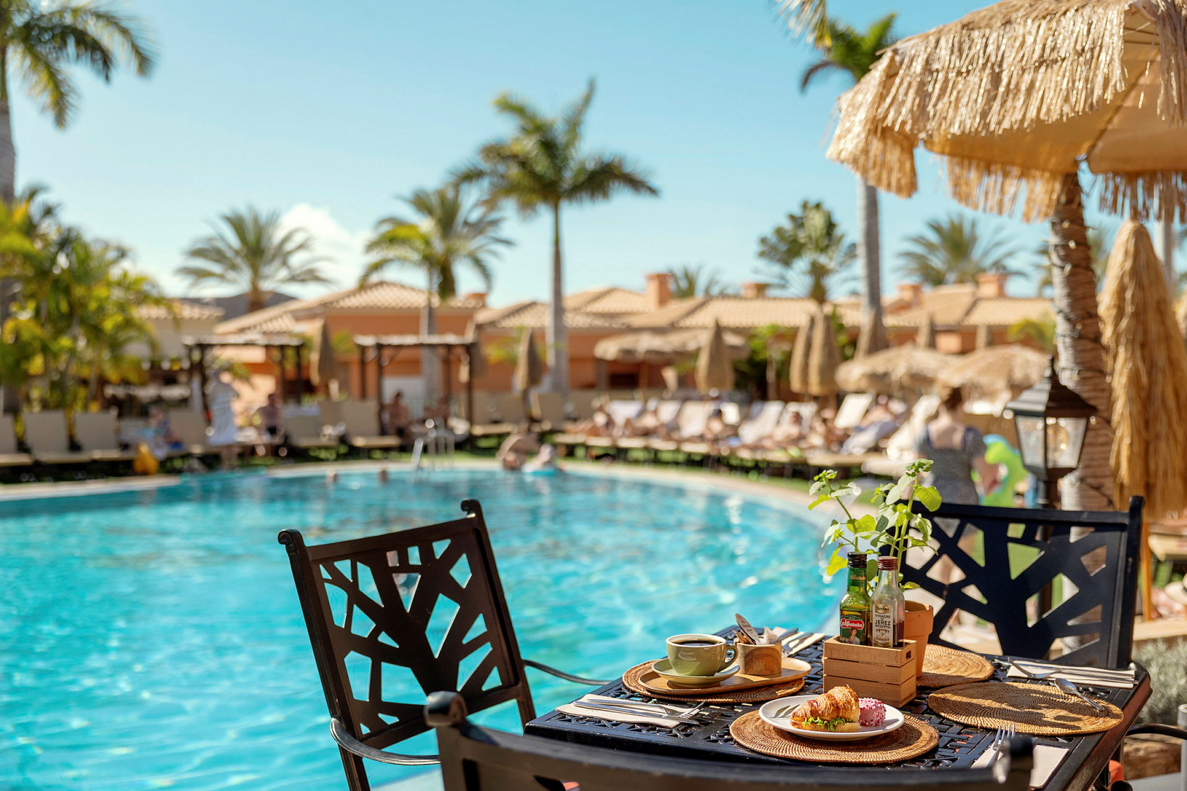 Frukost serverad vid ett bord intill en pool med solstolar och parasoller i bakgrunden. (AI-genererad text)