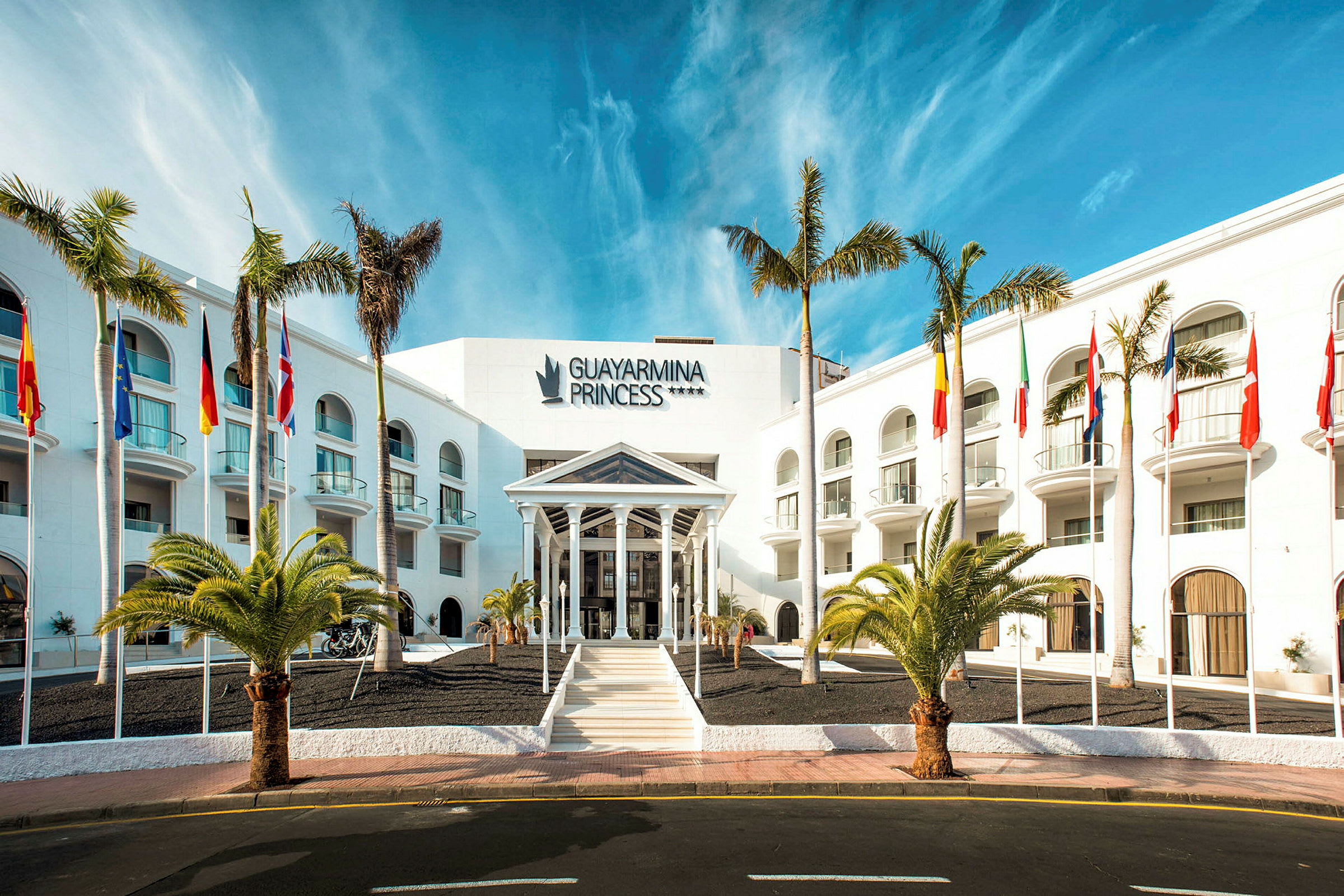 Hotell Guayarmina Princess med palmer och flaggor vid ingången. (AI-genererad text)