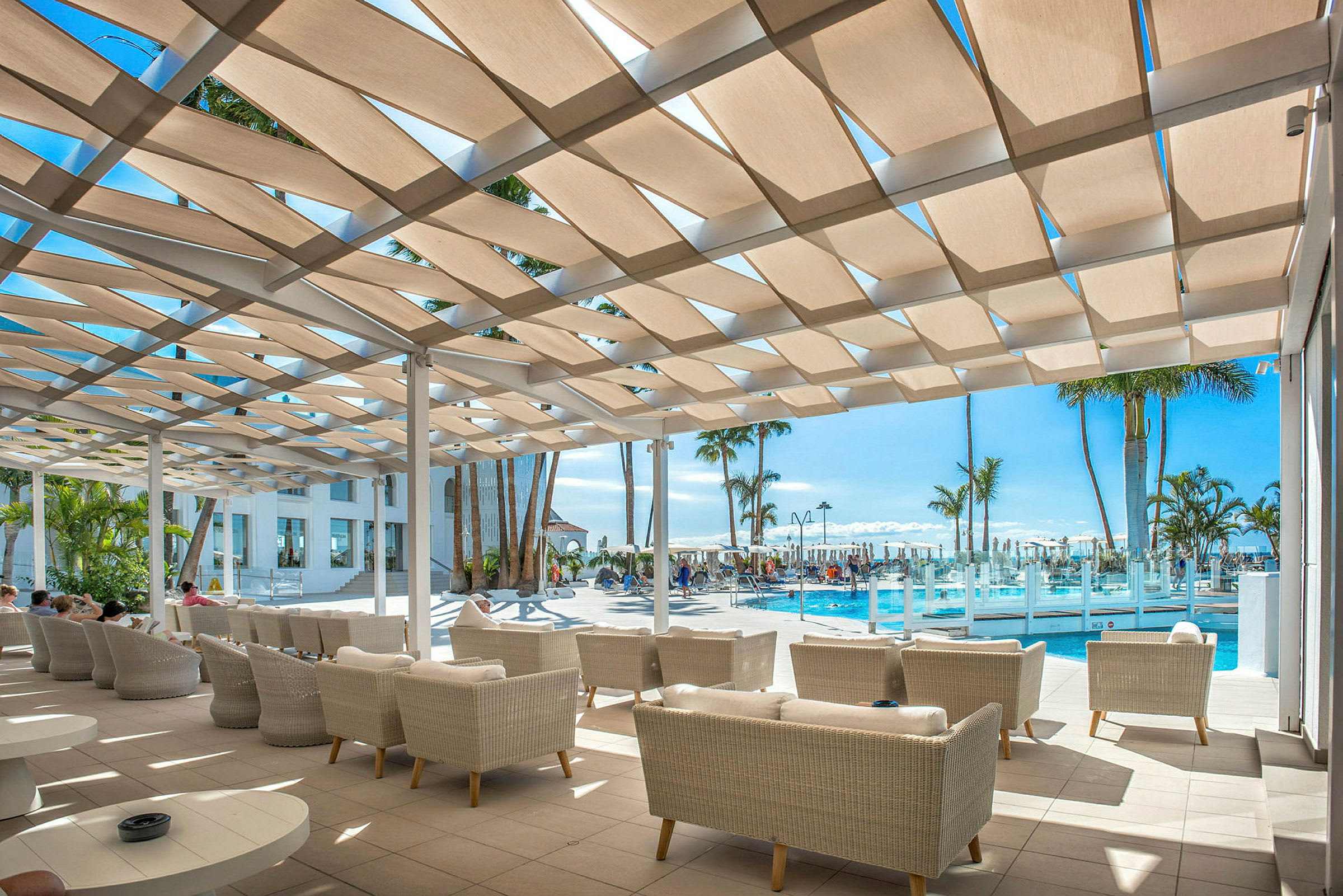 Loungeområde med soffor under en skuggande pergola vid en pool. (AI-genererad text)