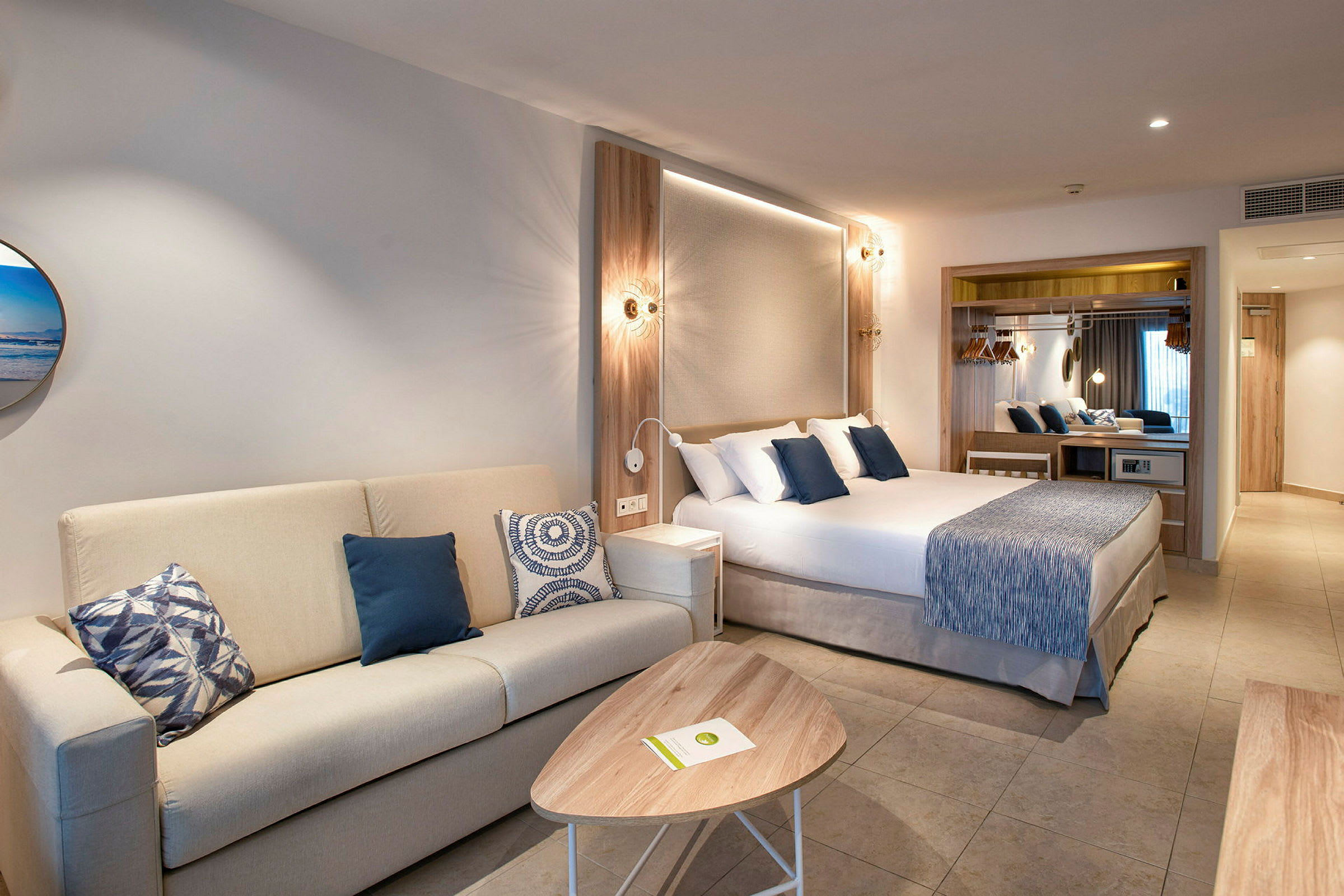 Ett hotellrum med en soffa, ett soffbord och en säng med blå dekorativa kuddar. (AI-genererad text)