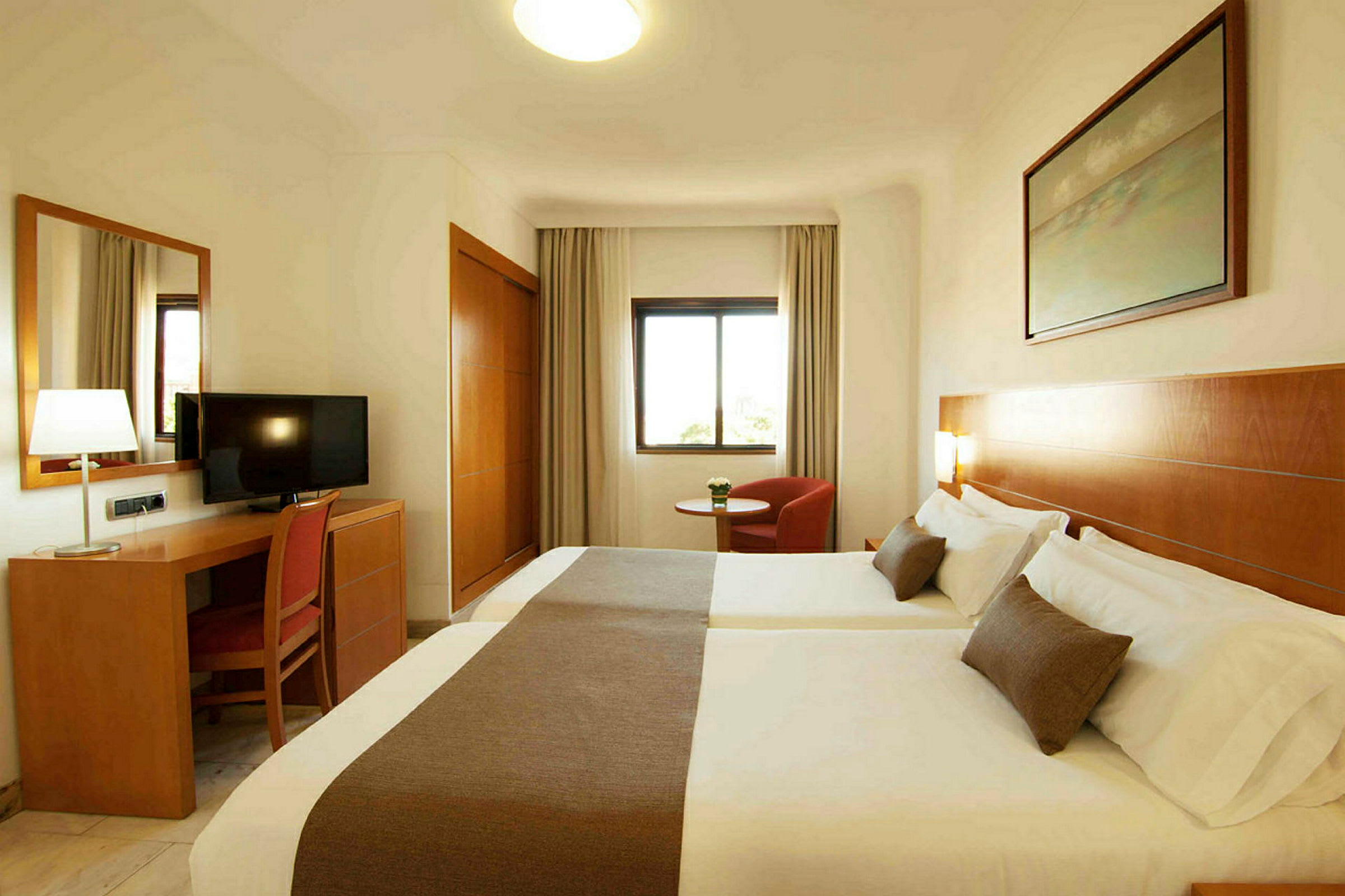 Ett hotellrum med två sängar, ett skrivbord med en stol och en TV, samt ett fönster och en fåtölj. (AI-genererad text)