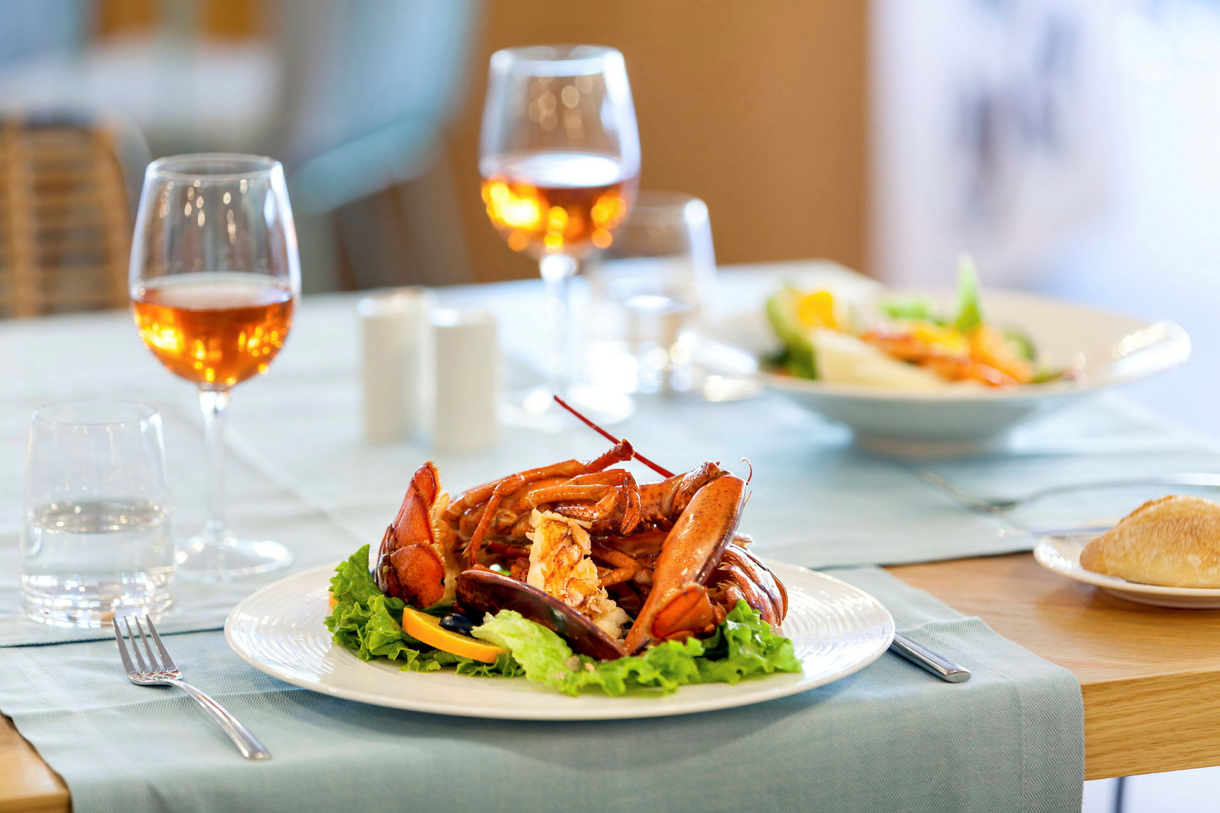 Ett dukat bord med en tallrik hummer och sallad, två glas orange vin samt brödförrätt. (AI-genererad text)