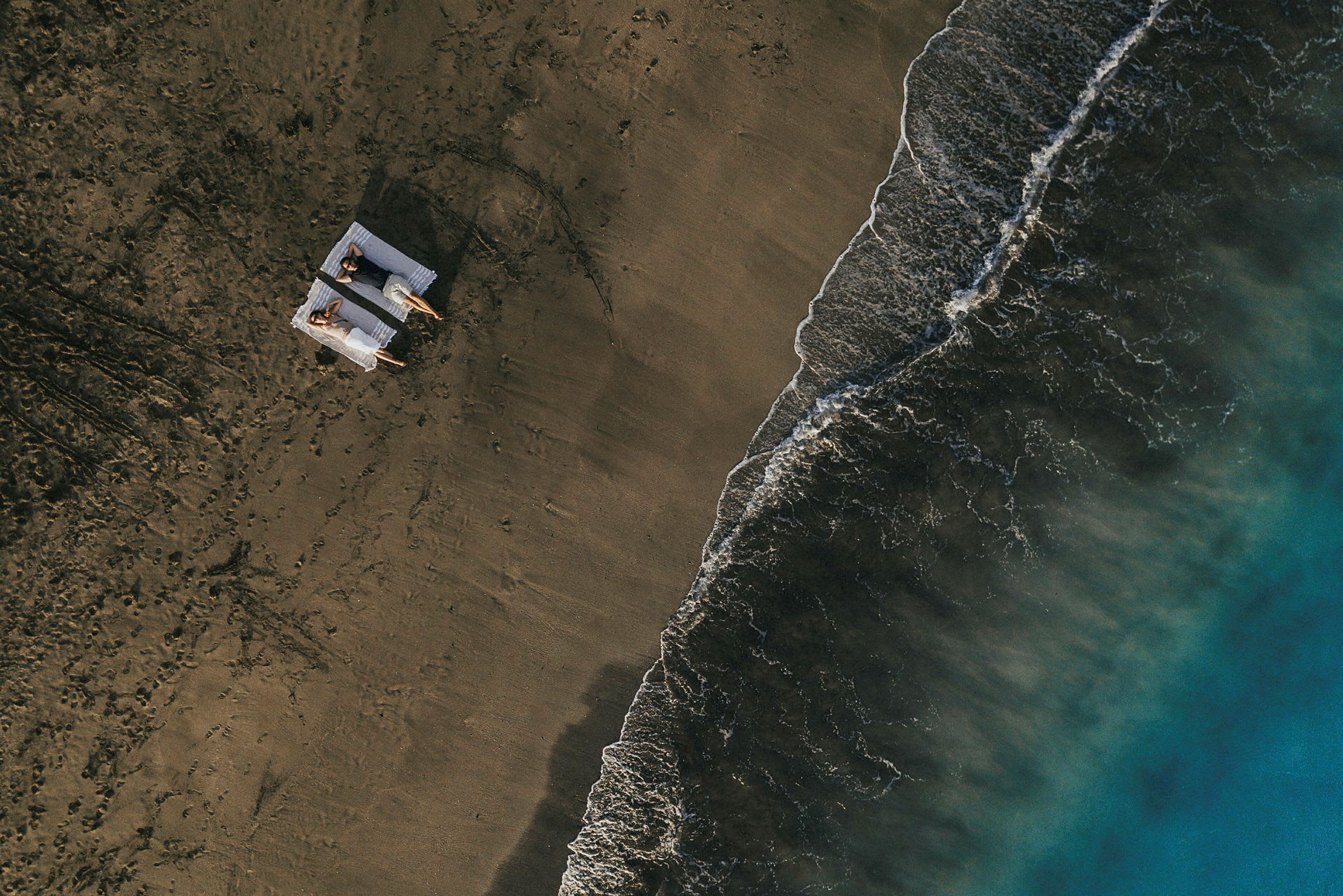 Två personer ligger på solstolar på en sandstrand bredvid havet. (AI-genererad text)