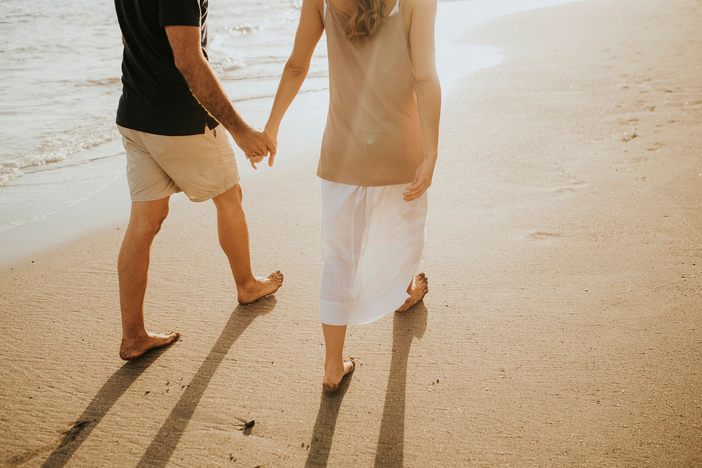 Två människor promenerar hand i hand på en solbelyst strand. (AI-genererad text)