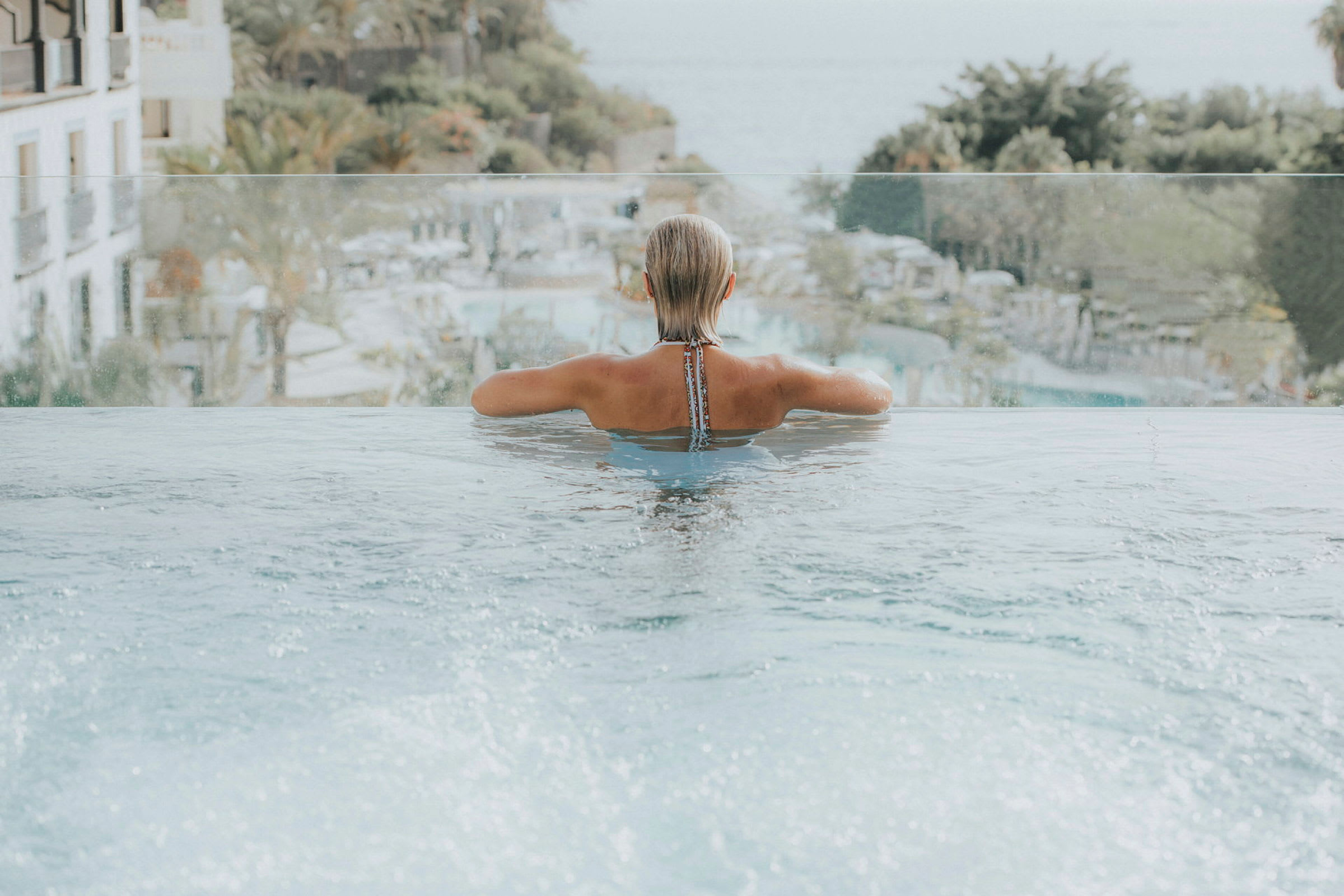 Person som badar i infinitypool med utsikt över natur och hotell. (AI-genererad text)