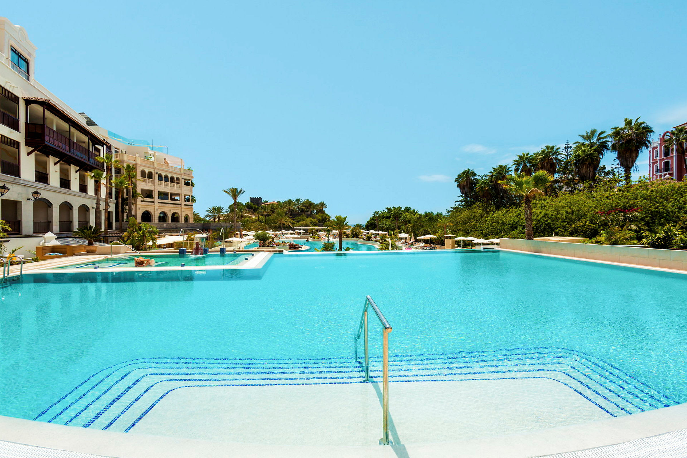 Stor swimmingpool vid ett hotell med omgivande grönska. (AI-genererad text)