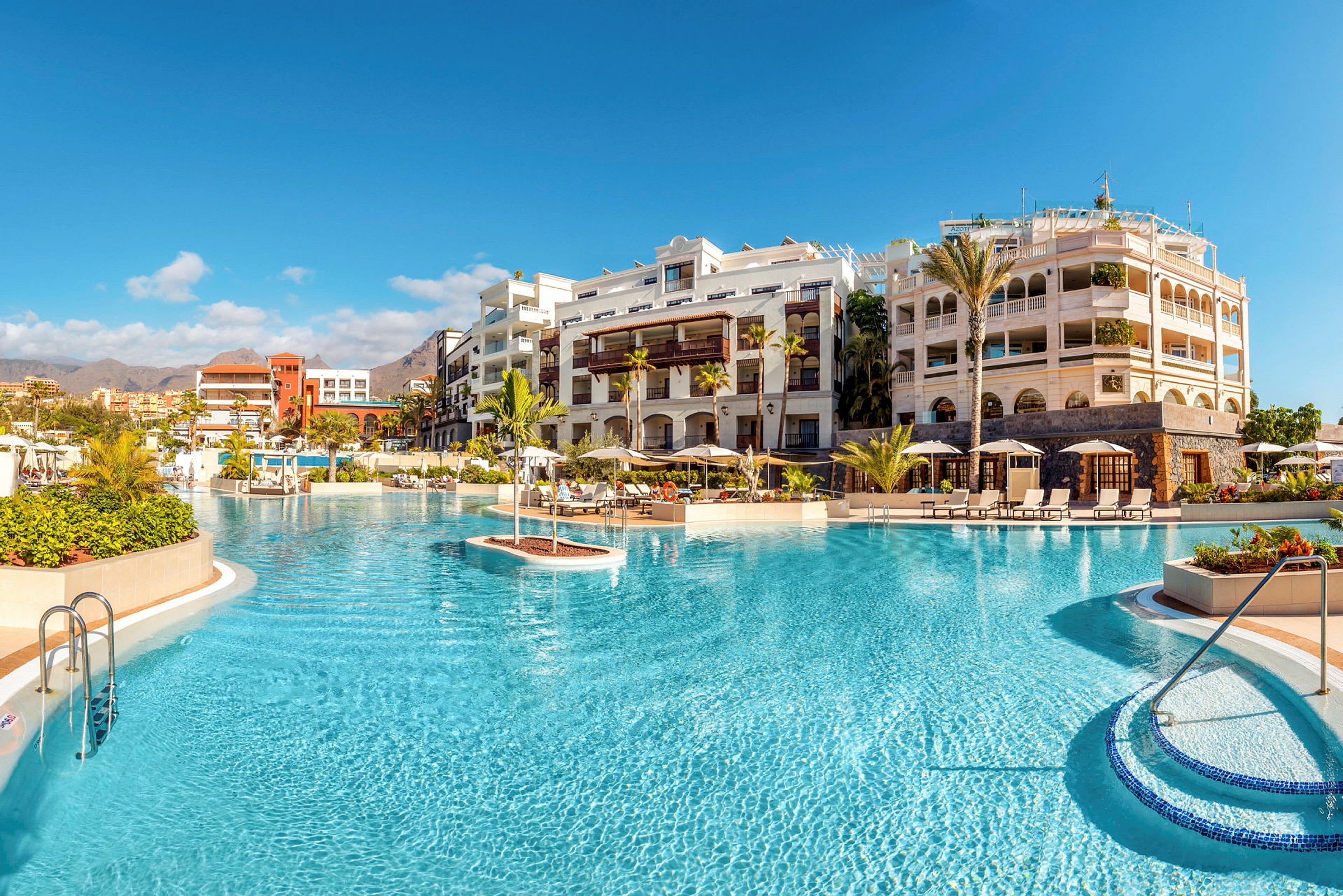 Bild av en lyxig hotellpool med solstolar och parasoller, omgiven av eleganta byggnader. (AI-genererad text)