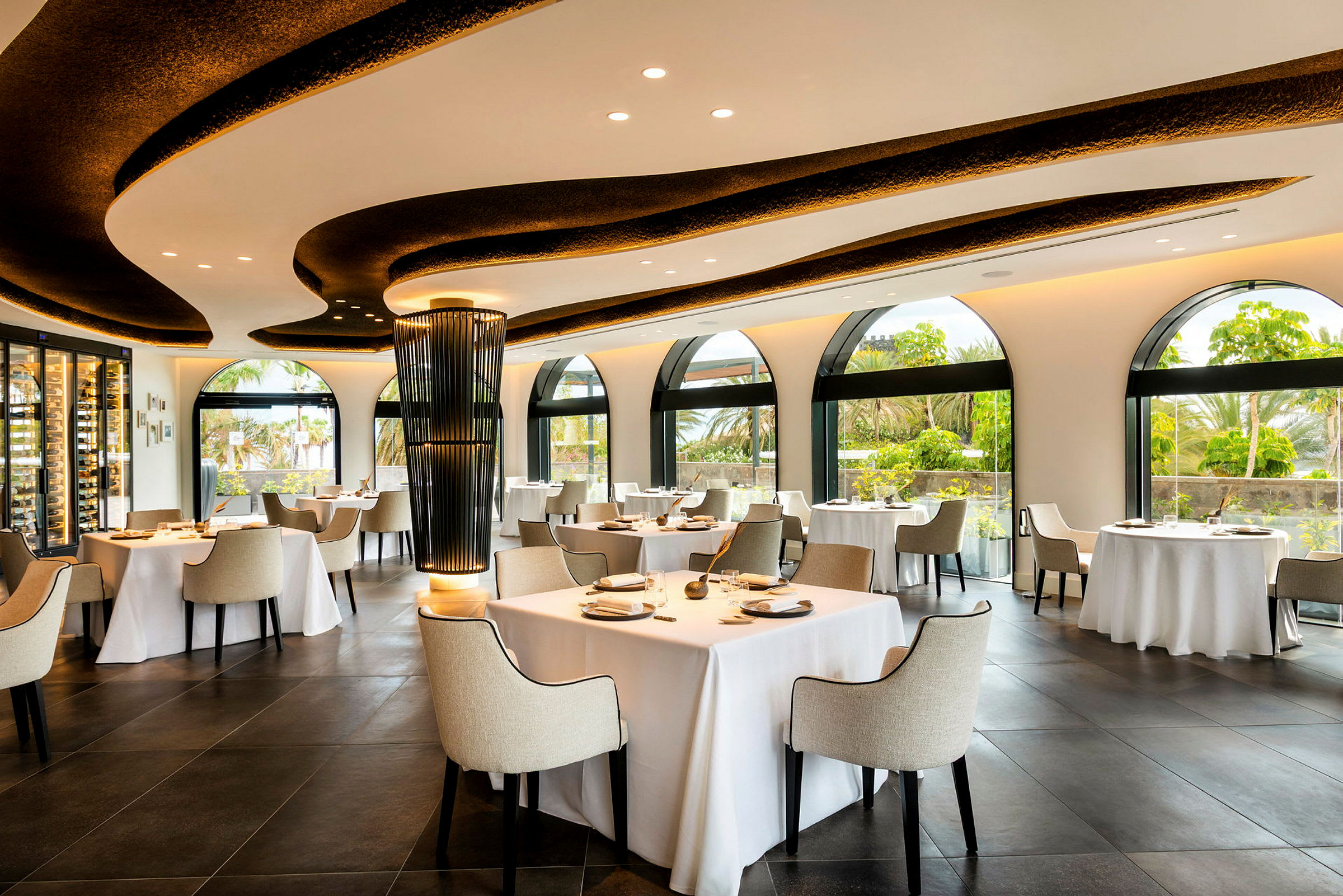 Restaurang med ljus inredning, stora fönster, och dukade bord. (AI-genererad text)
