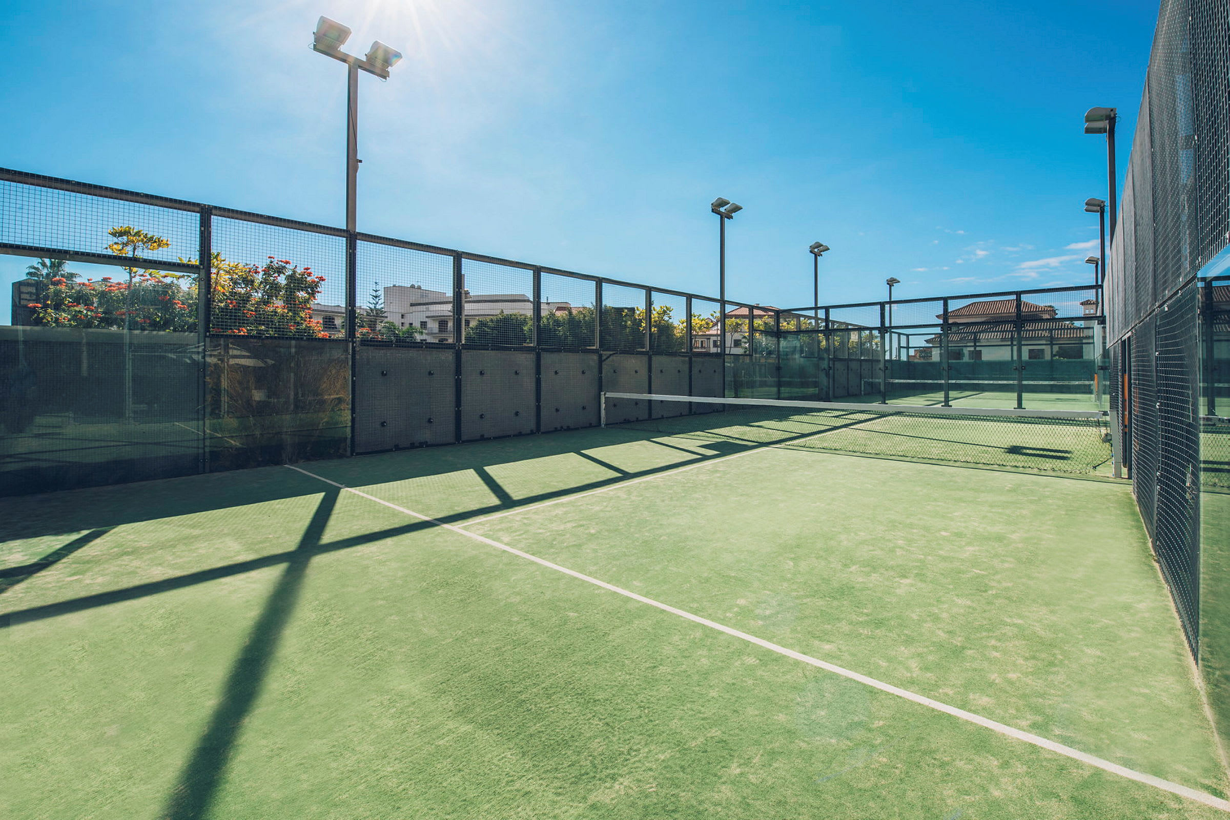 En utomhus padelbana med grönt underlag och omgiven av glas och nätstaket. (AI-genererad text)