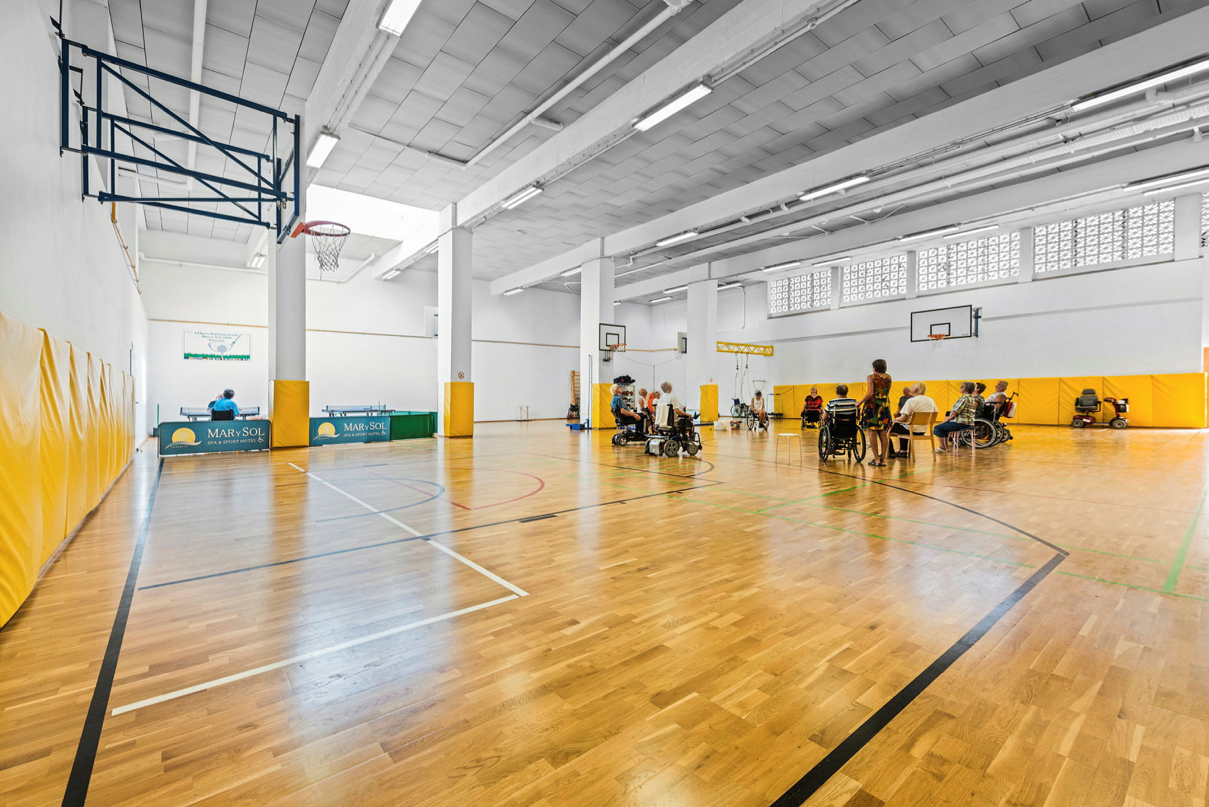 En sporthall med personer i rullstolar som deltar i gruppaktiviteter. (AI-genererad text)