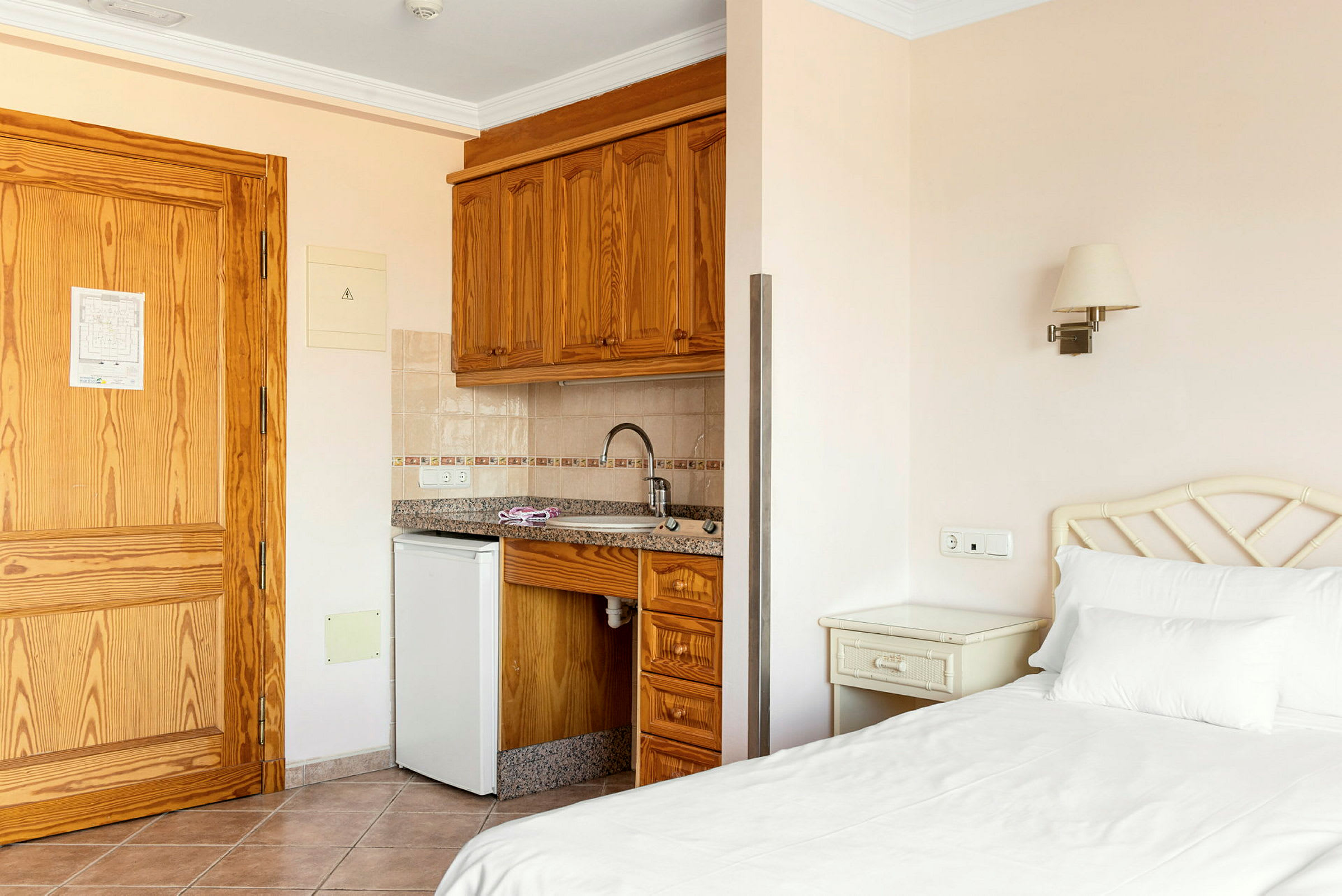 Hotellrum med säng, nattduksbord, köksutrustning och träinredning. (AI-genererad text)