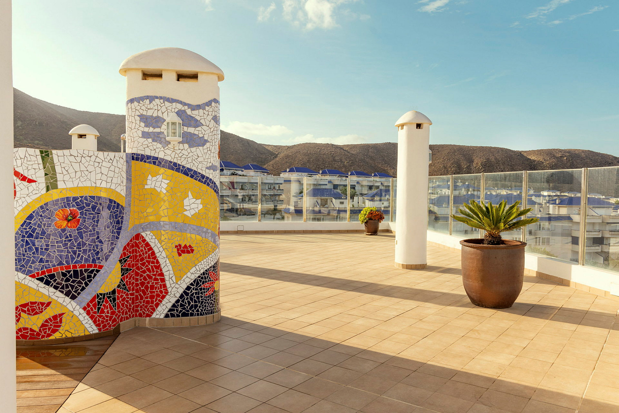 Exteriör av en terrass med keramisk mosaik, krukväxter och berg i bakgrunden. (AI-genererad text)