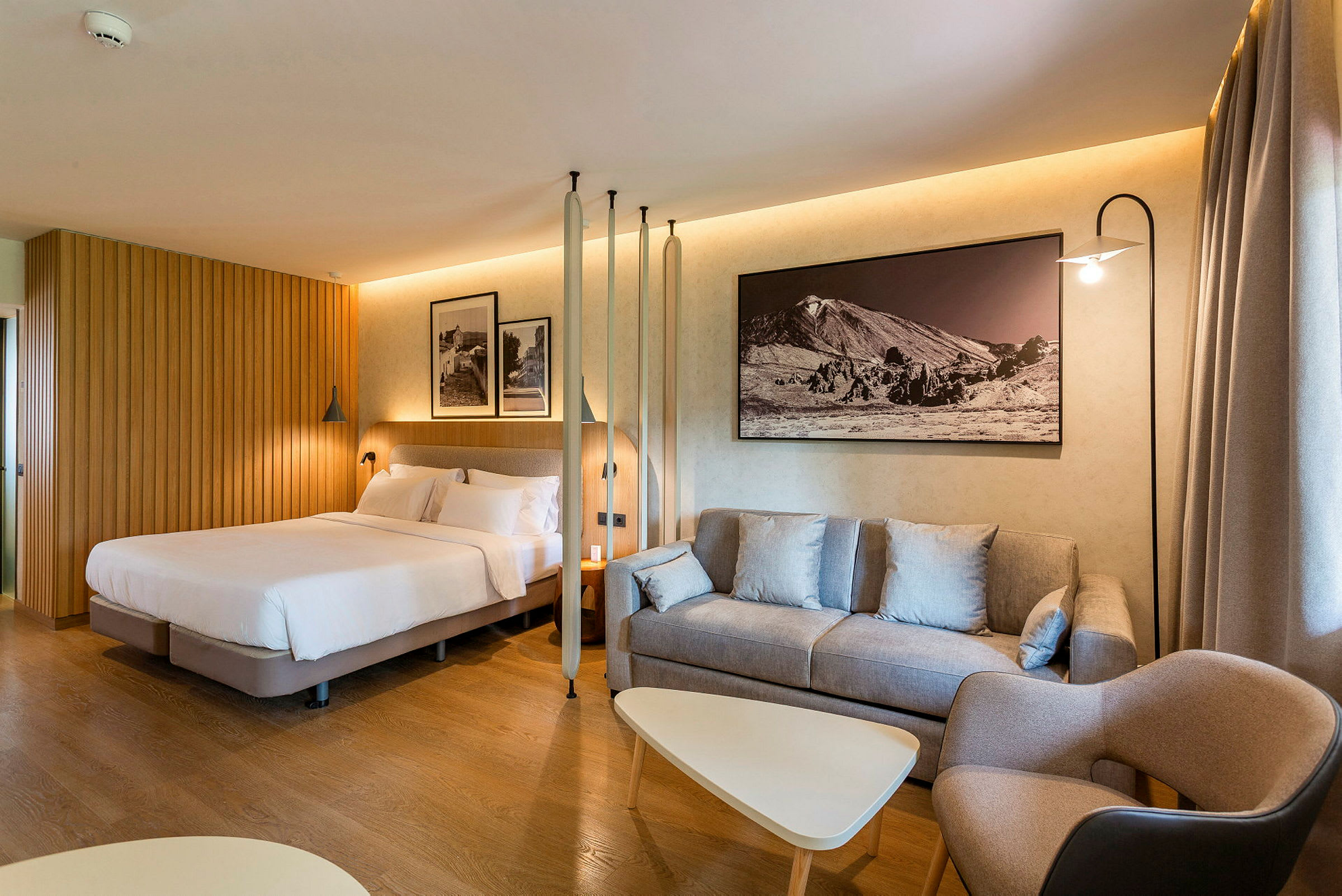 Hotellrum med säng, soffa och bord samt väggdekoration. (AI-genererad text)