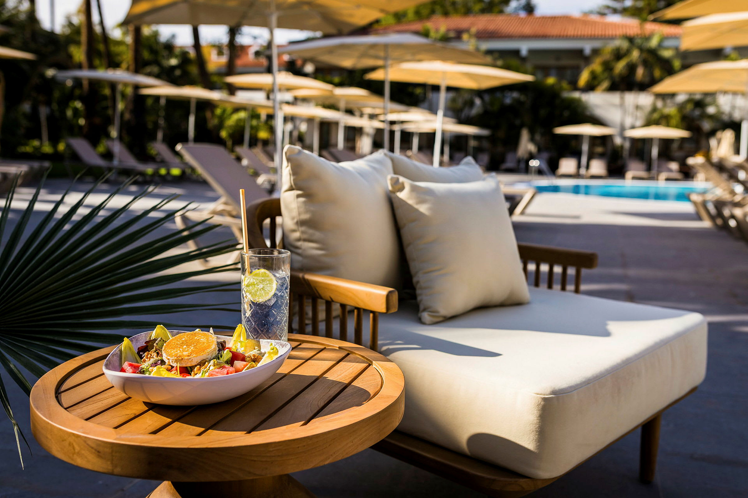 Ett bord med en sallad och en drink bredvid en solstol vid en pool. (AI-genererad text)