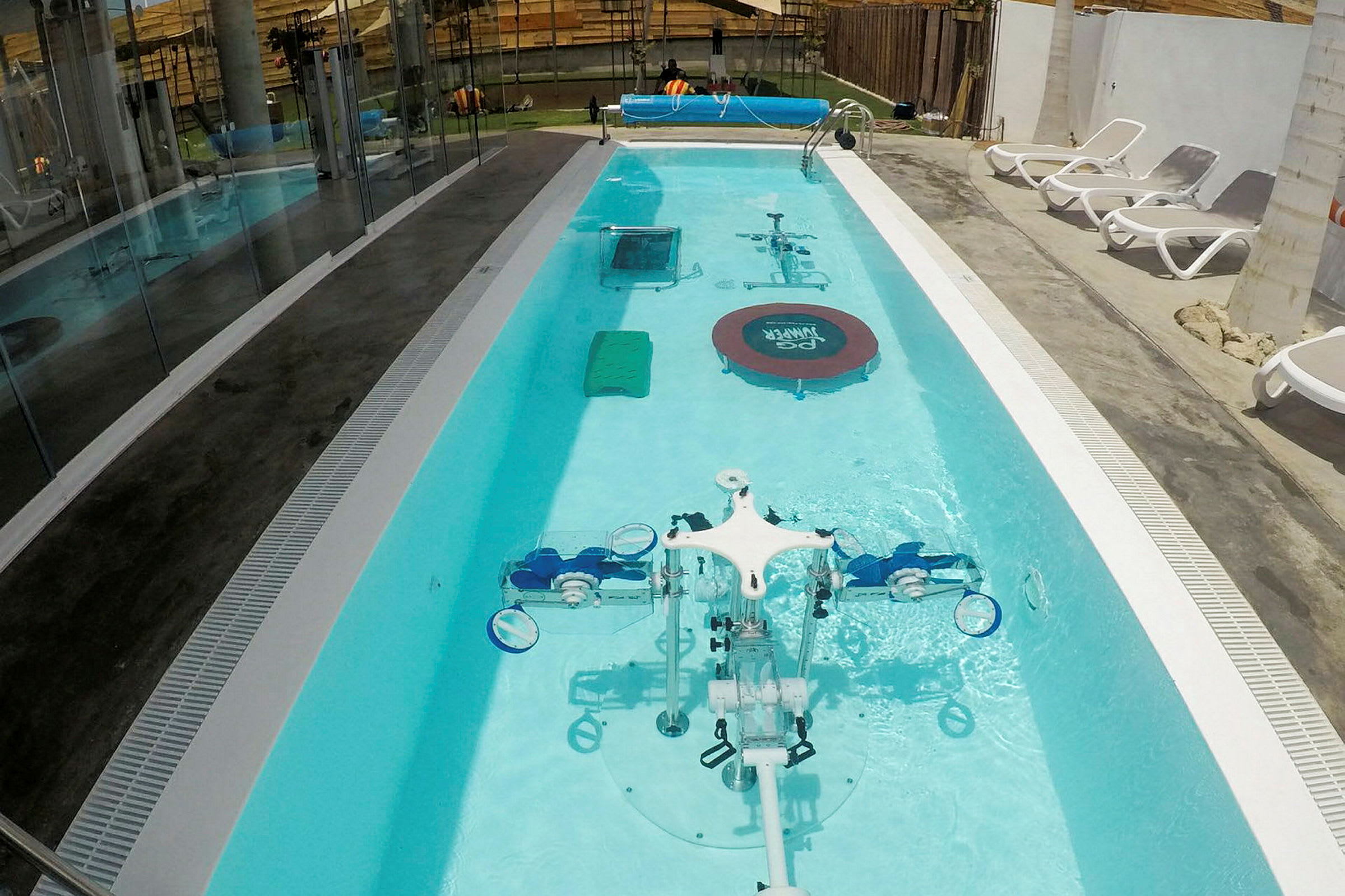 En smal pool utomhus med utrustning för dykträning ligger bredvid solstolar. (AI-genererad text)