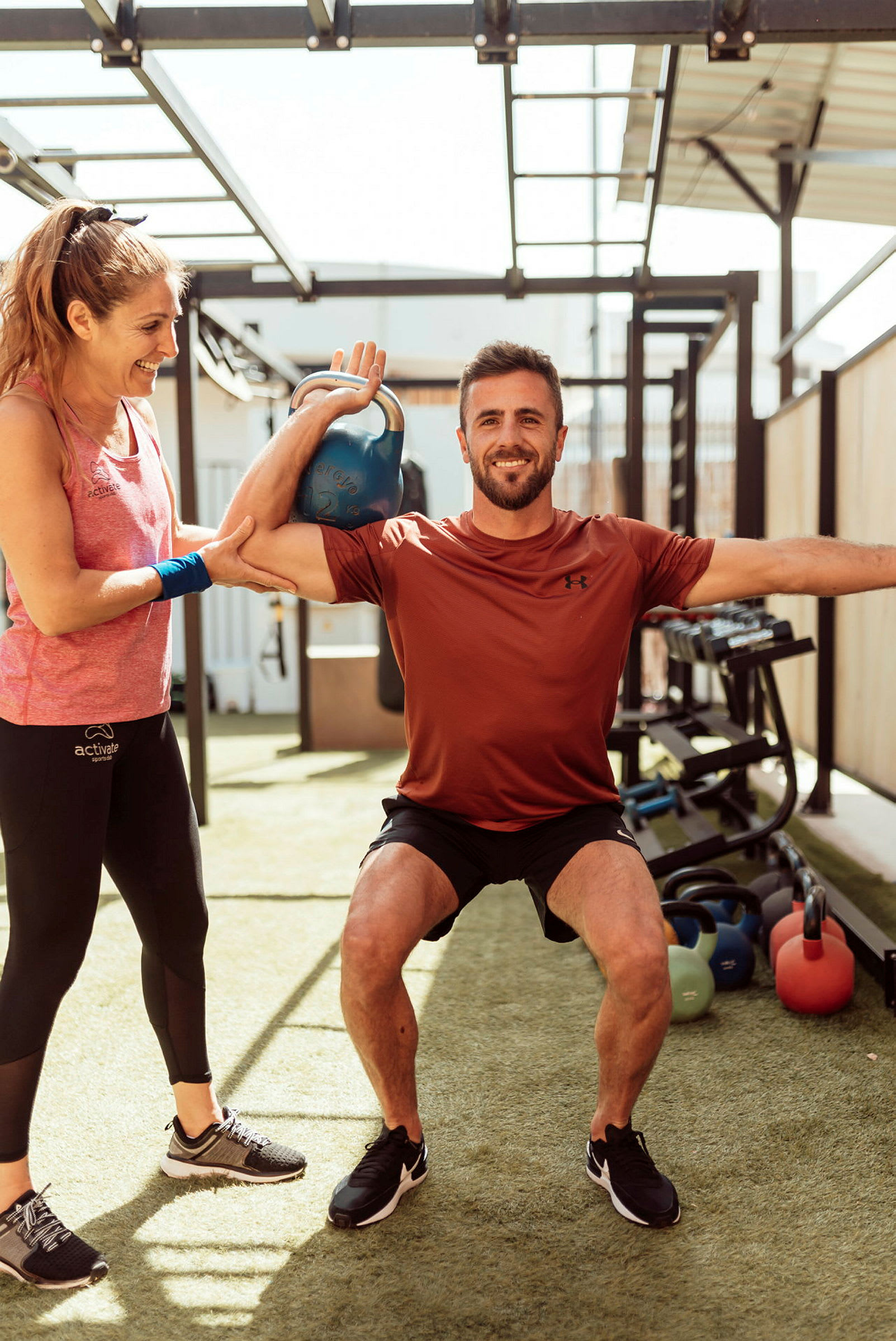 Person tränar med kettlebell och får assistans utomhus. (AI-genererad text)
