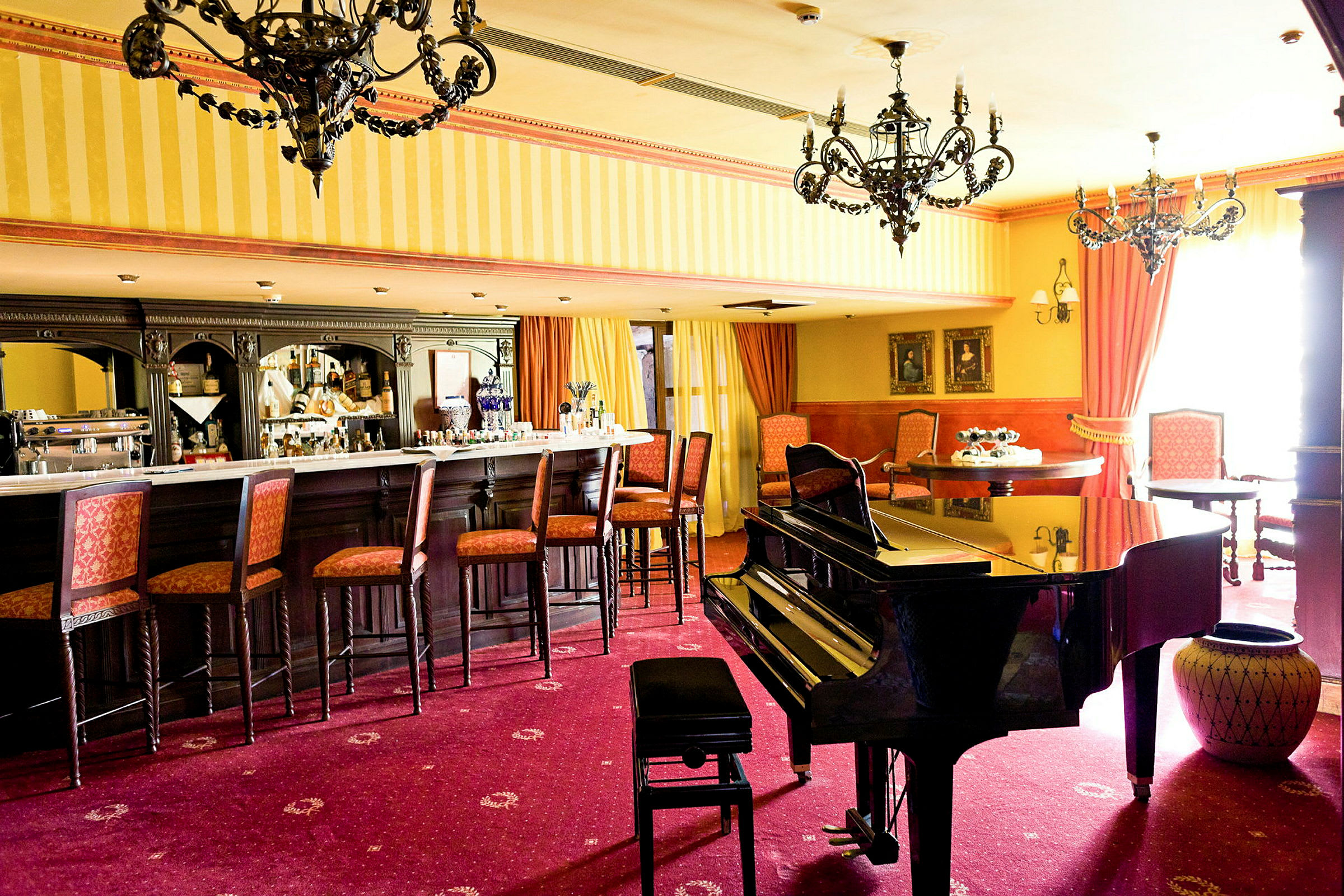 En barlounge med stolar vid bardisken, ett piano i förgrunden och eleganta ljuskronor i taket. (AI-genererad text)