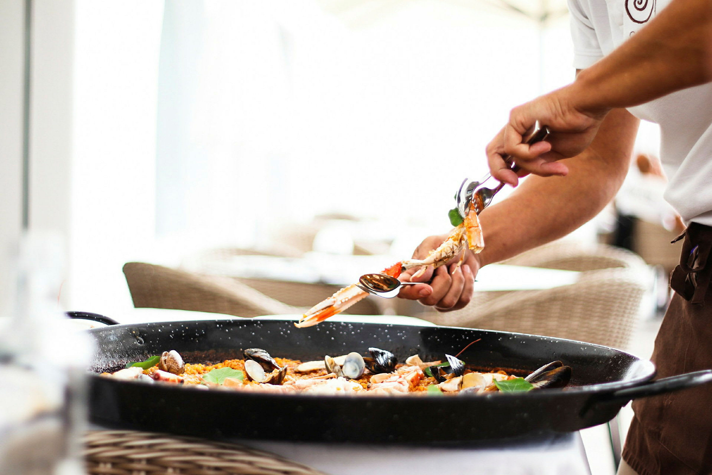 En person lägger mat från en paellapanna med ett serveringsverktyg. (AI-genererad text)