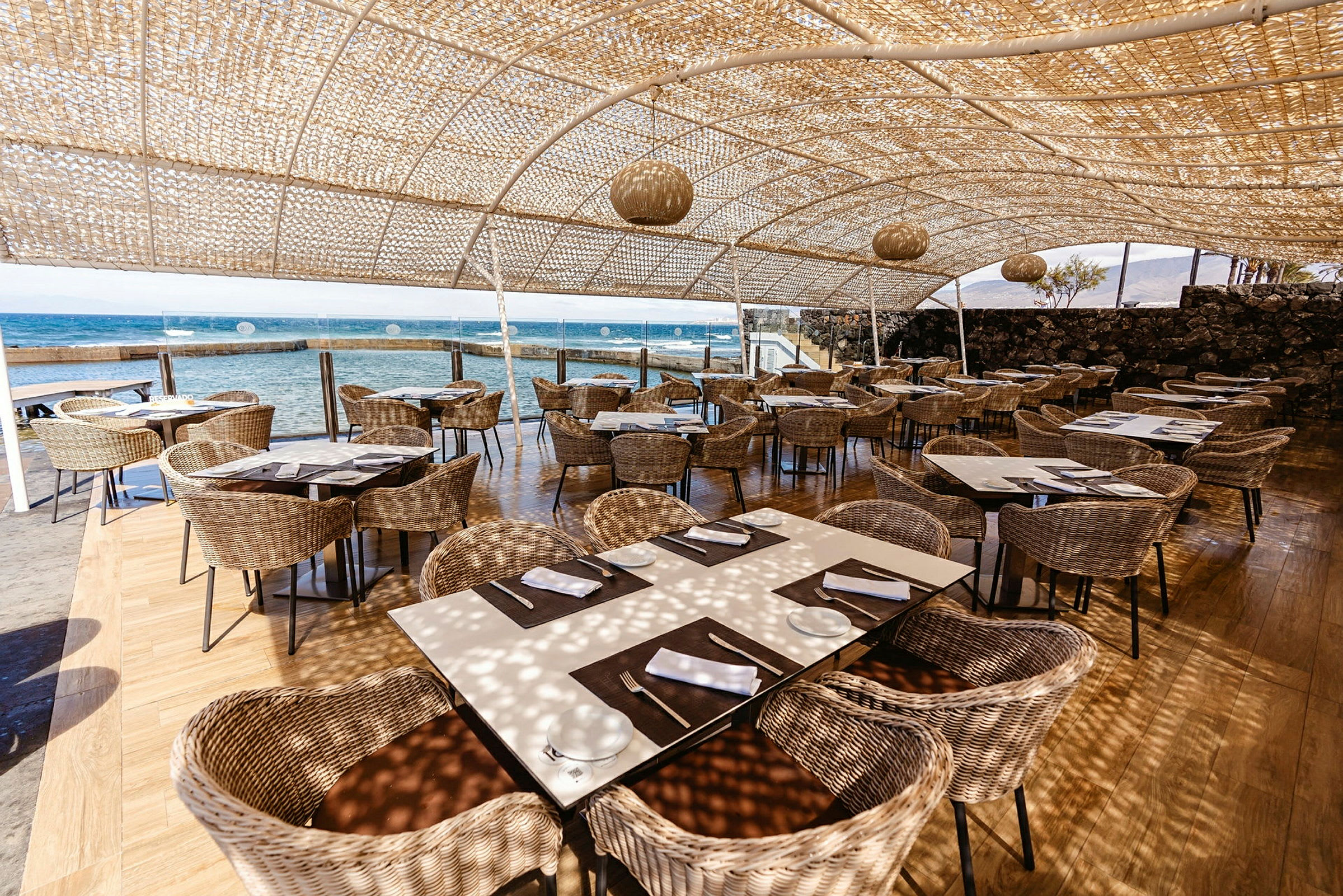 Utomhus restaurang med sittplatser av rotting och utsikt över havet. (AI-genererad text)