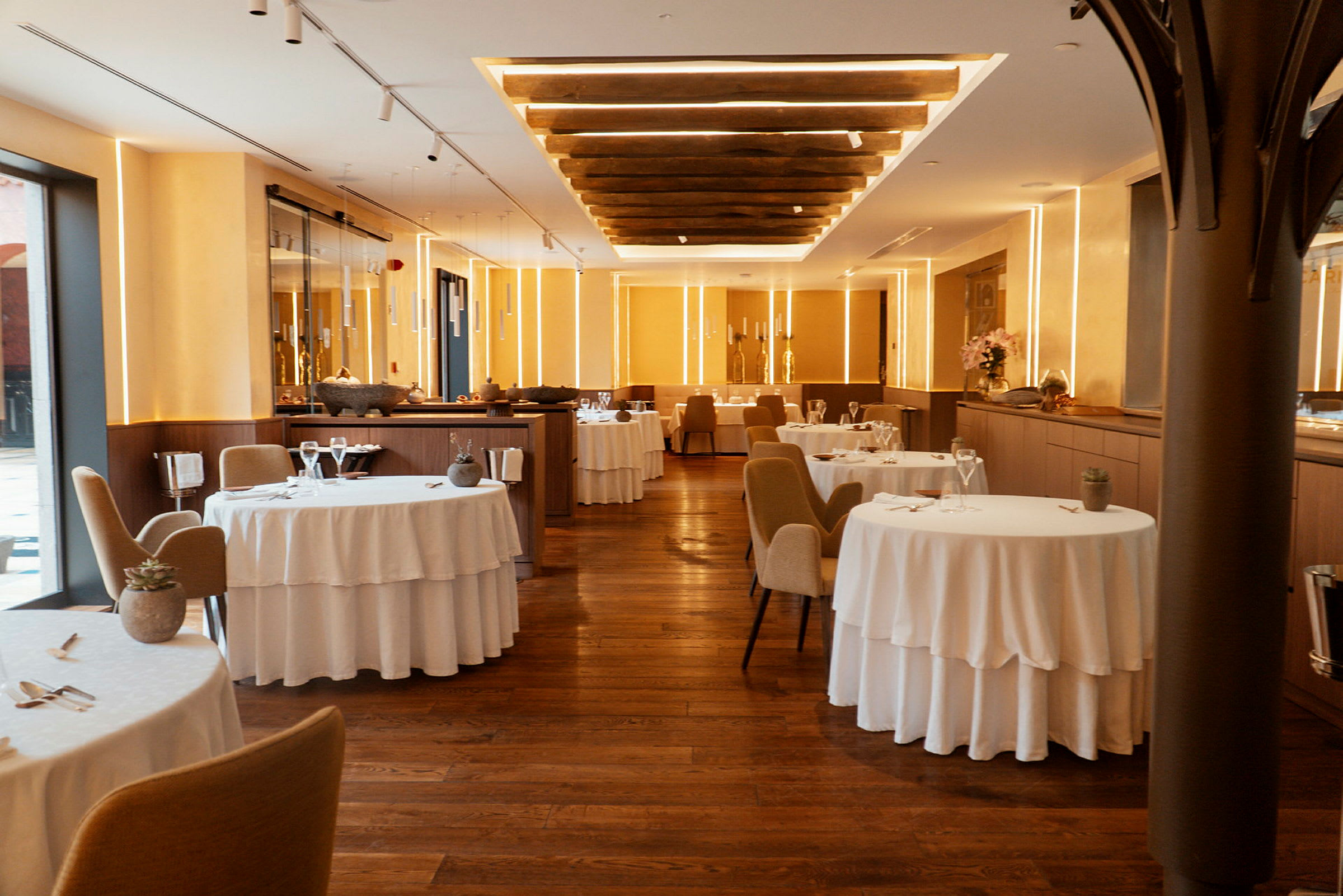 Ett elegant inrett restaurangutrymme med vita dukar, trästolar och varm belysning. (AI-genererad text)