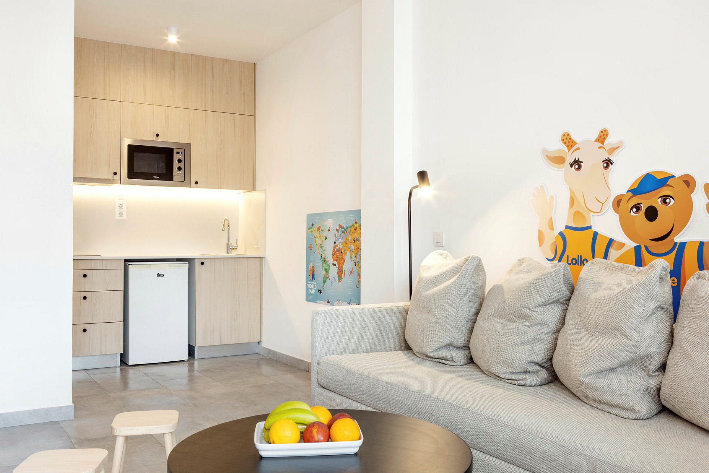 Bild på ett litet kök med trämöbler, soffa med grå kuddar, samt dekoration med giraff- och björnfigurer på väggen. (AI-genererad text)