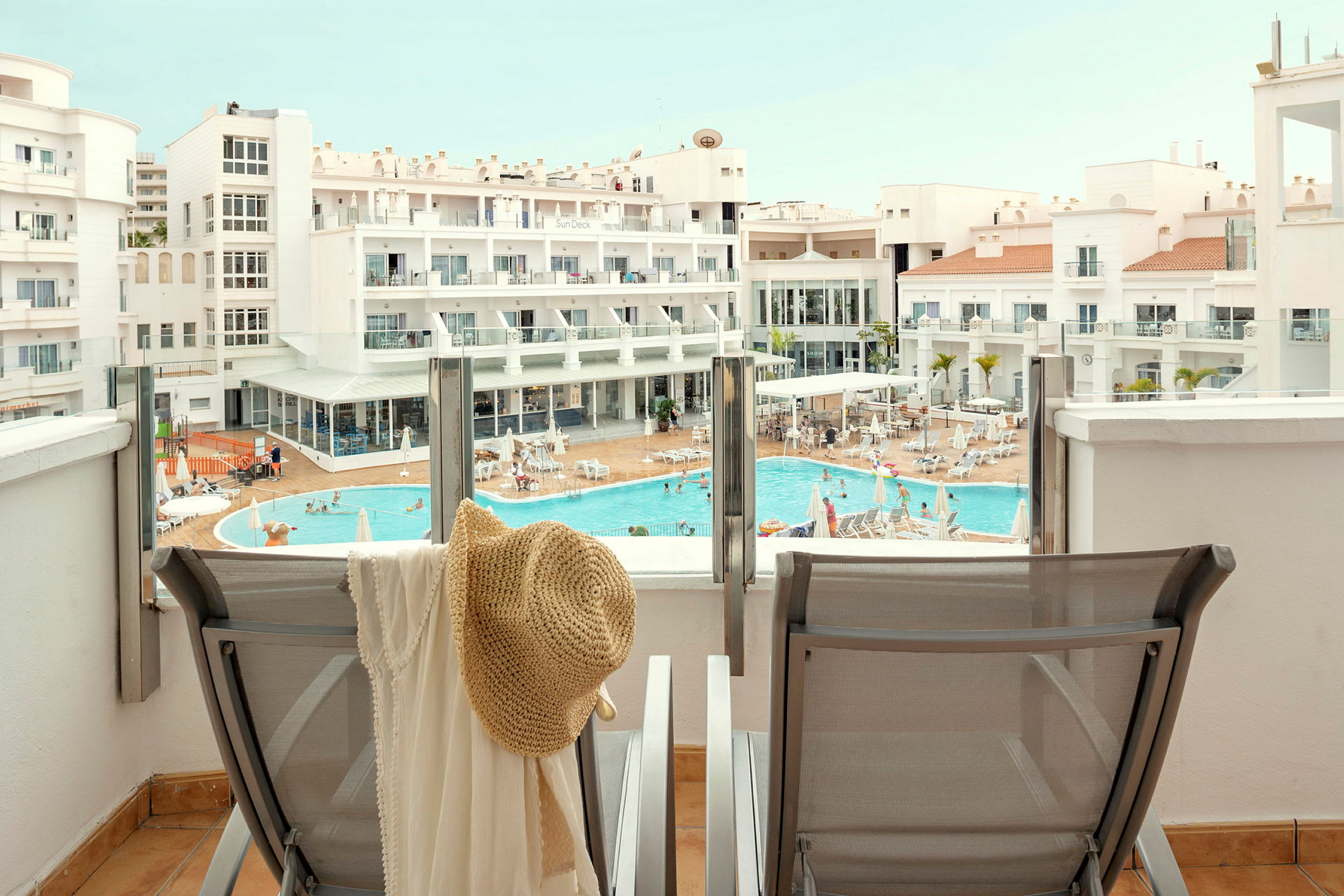 Utsikt från en terrass mot en pool och hotellbyggnad. (AI-genererad text)