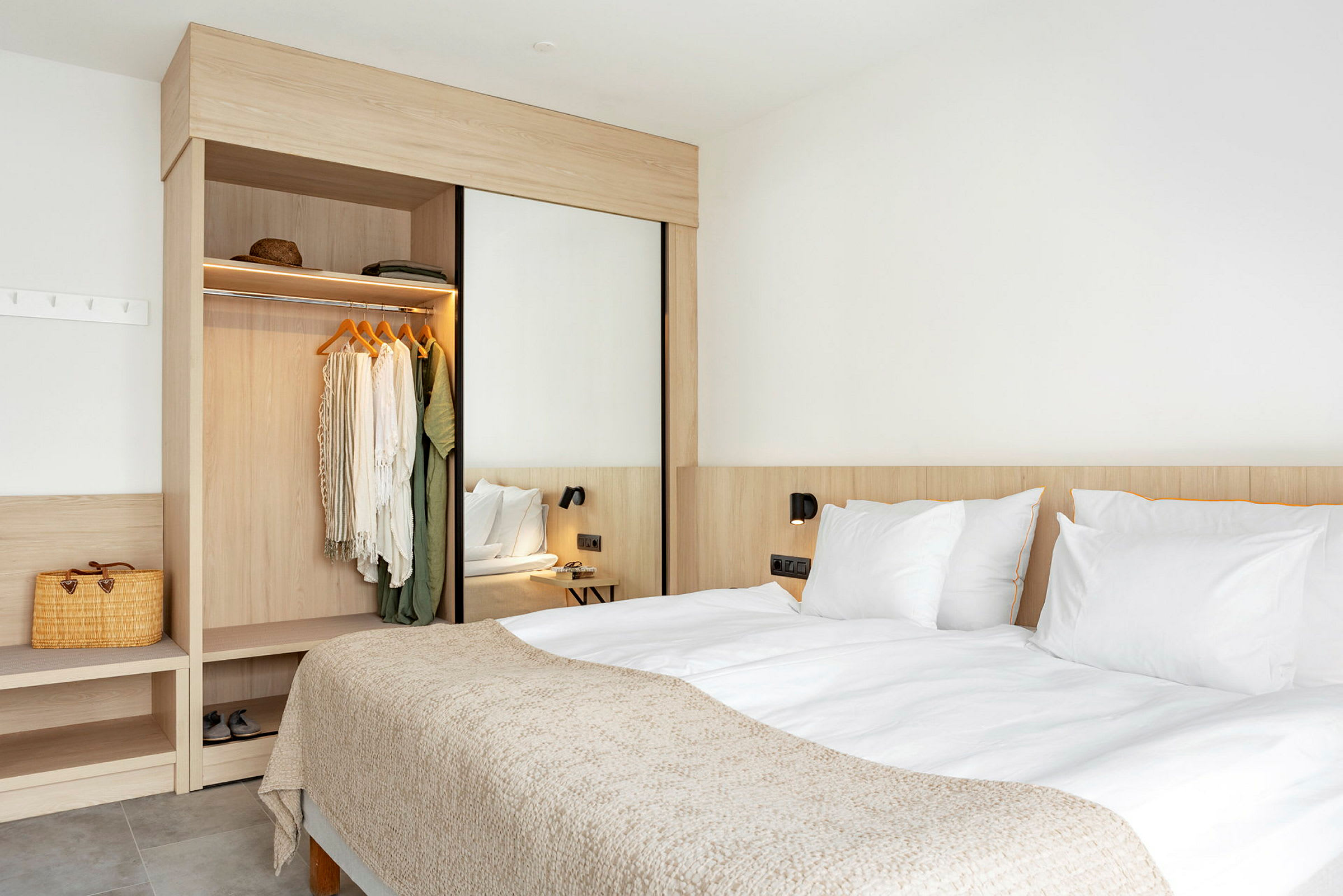 Ett hotellrum med en dubbelbädd, ett öppet garderobsutrymme och en väggkrok med väska. (AI-genererad text)