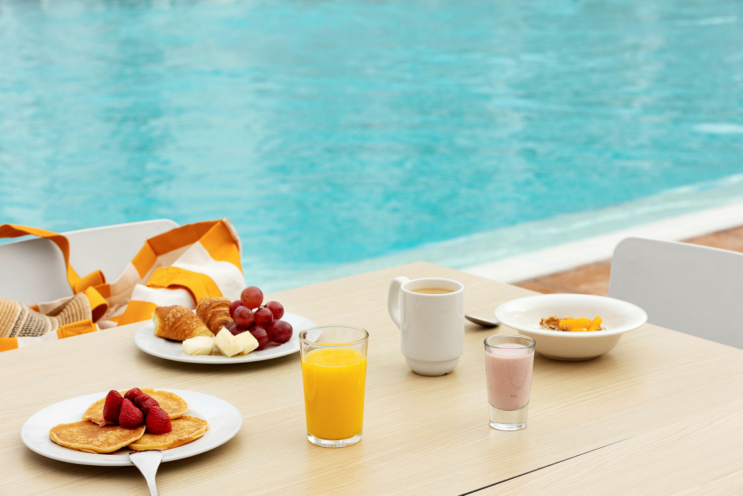 Frukost med frukt, pannkakor, juice och kaffe på ett bord vid en pool. (AI-genererad text)