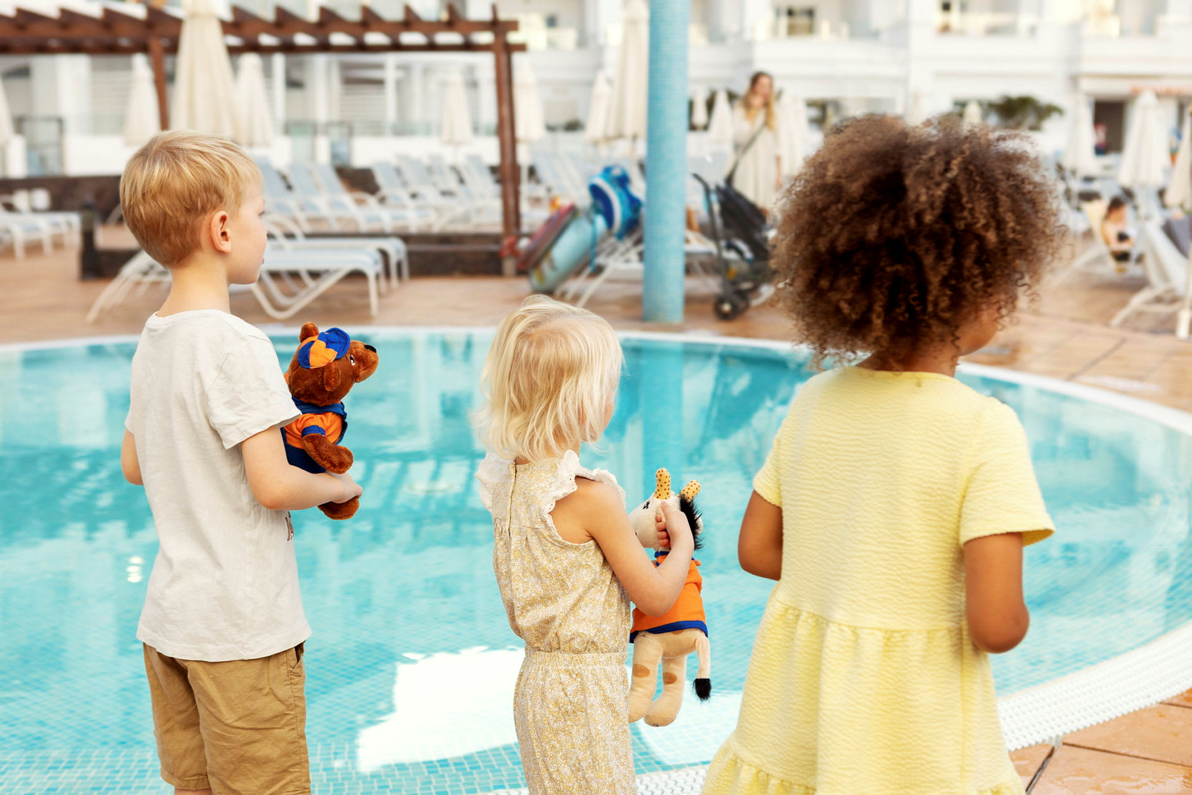 Barn står vid en pool och håller i gosedjur. (AI-genererad text)