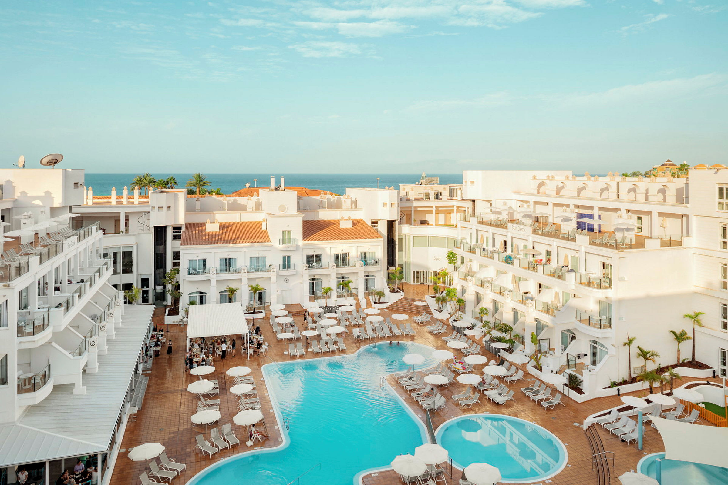 Vy över hotellområde med pool och solstolar, havet syns i bakgrunden. (AI-genererad text)