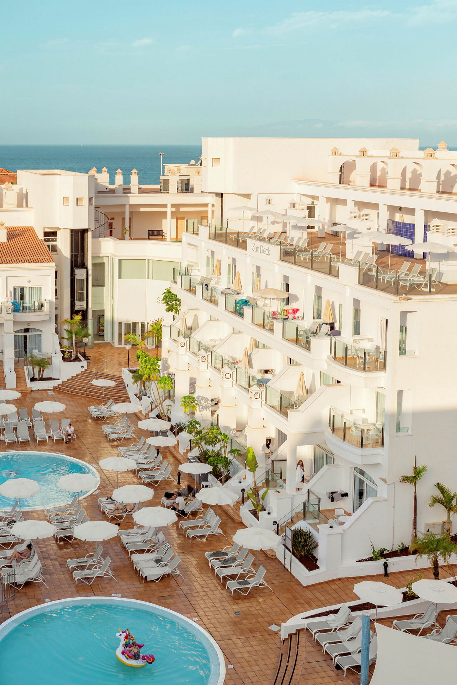 Bilden visar ett hotellområde med en pool och solstolar samt vita byggnader i bakgrunden. (AI-genererad text)